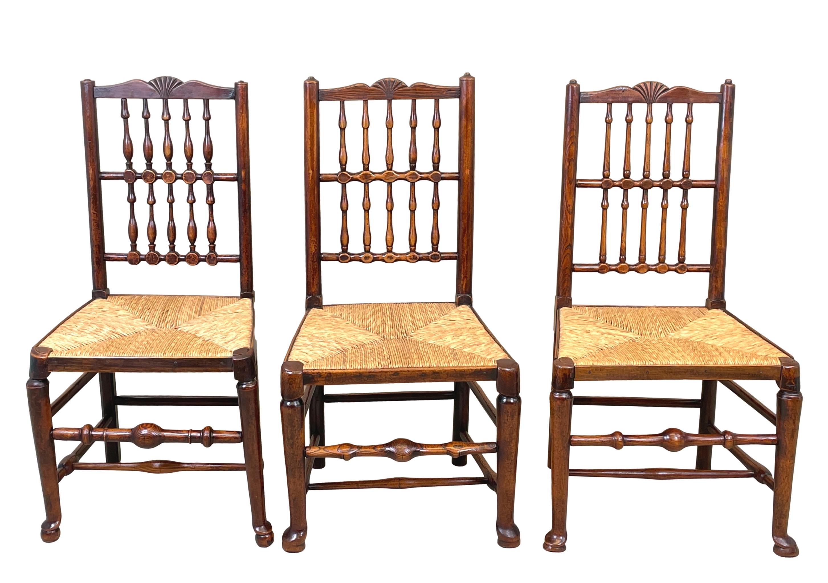 A charming matched set of six early 19th century, English ash and elm, country farmhouse design, dining chairs having elegant double row of spindles with central carved fan to backs over rushed seats raised on turned legs united by turned