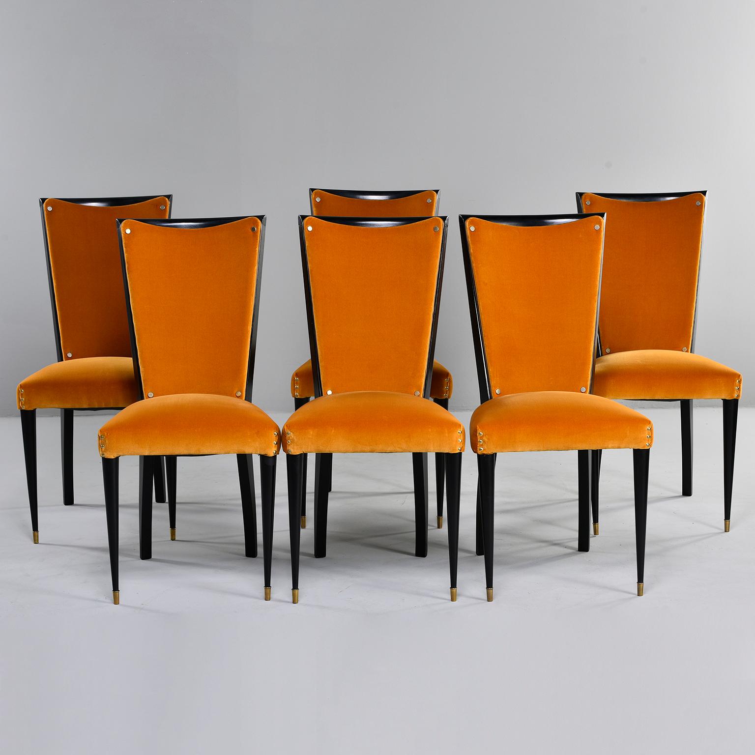 Set of six ebonised deco style dining chairs, circa 1940s. Chairs have tapered front legs with brass foot caps. Recently upholstered in poppy gold velvet that is in very good overall condition with virtually no signs of wear. Accented with brass