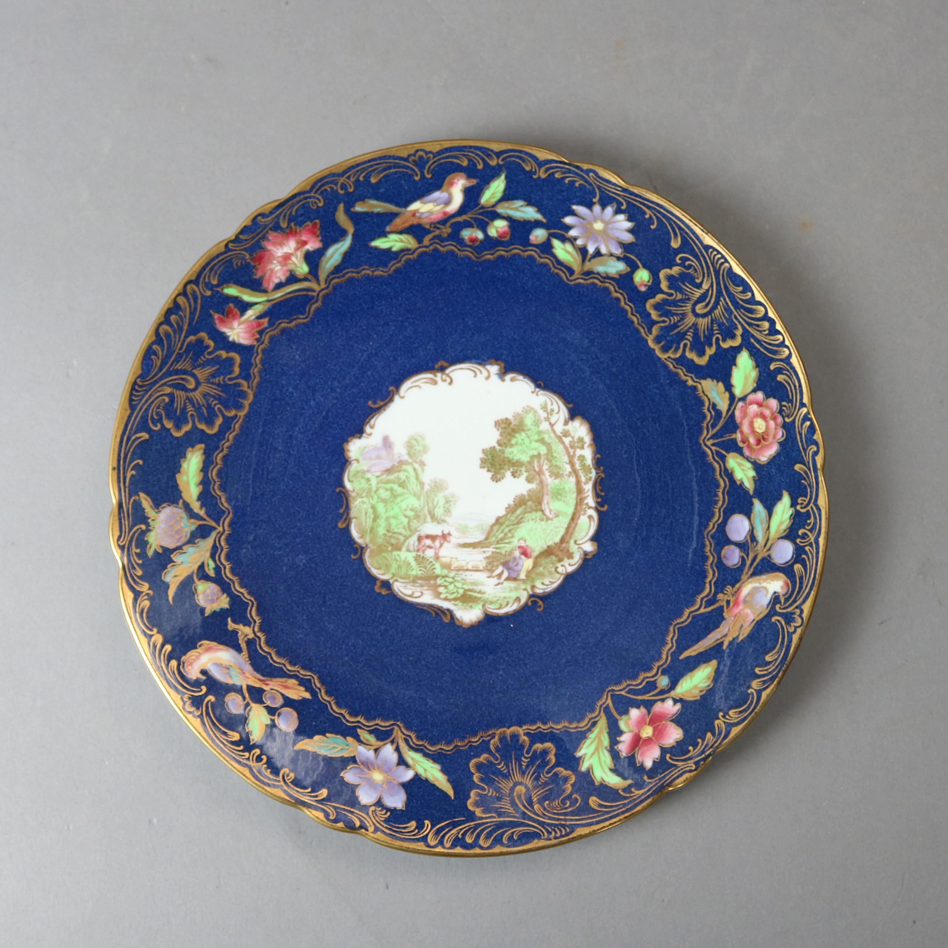A set of 6 English Copeland Spode pictorial plates offer central reserve with Scottish Irish countryside scene with structure, cow, stream and courting couple on cobalt blue ground with gilt scroll and foliate decoration, en verso maker mark, 20th