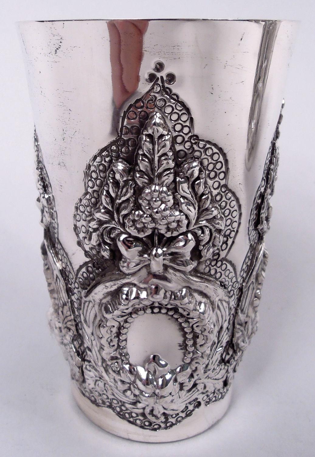 Set of 6 fancy sterling silver wine cups. Each: Straight and tapering sides. Vertical pattern in relief comprising beaded rondels (vacant) surrounded by leaf-wrapped reeded frame and surmounted by ribboned leaves and flowers on stippled multifoil