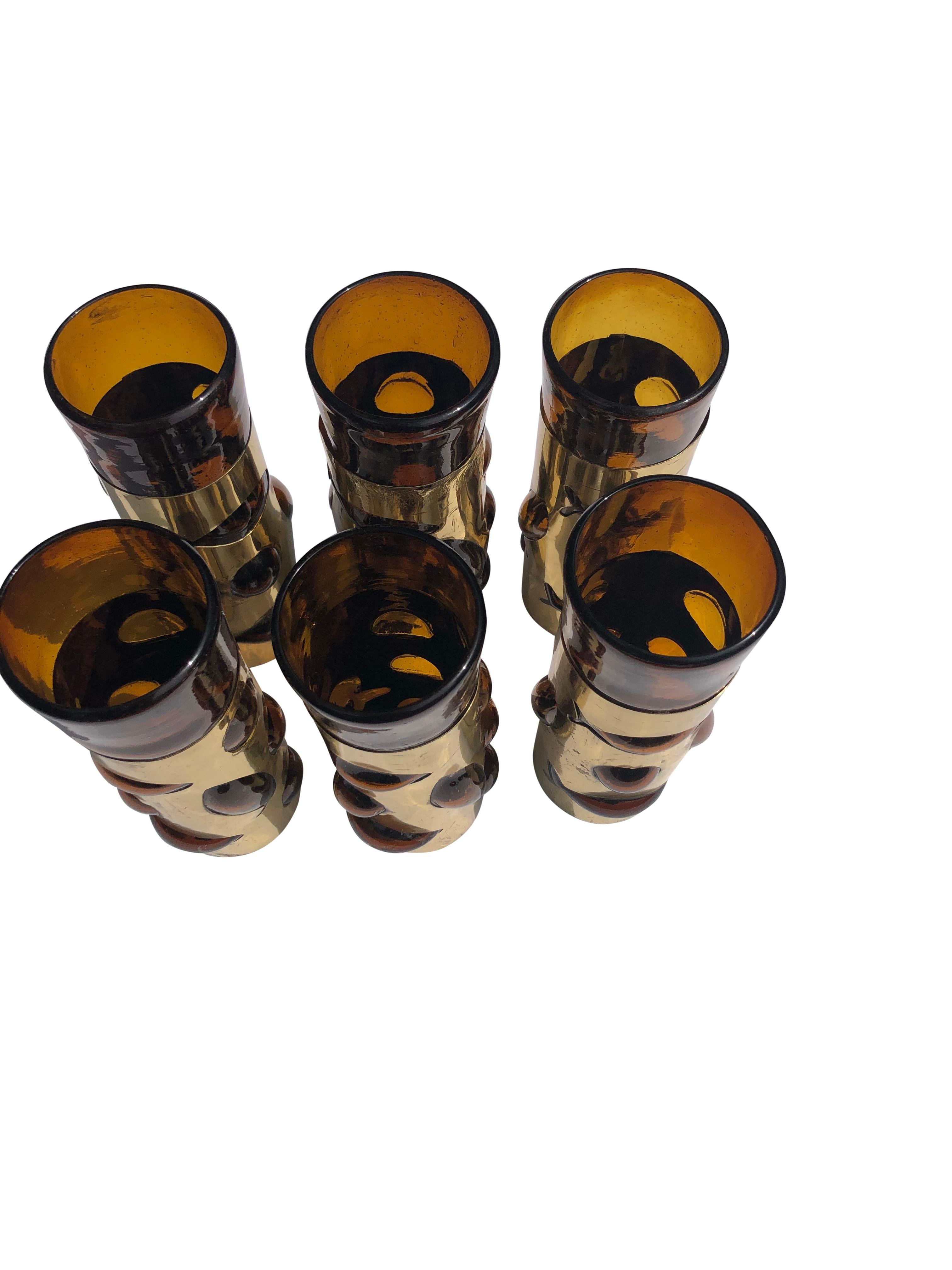 Set of 6 Tall Tom Collins glasses by Mexican artist Felipe Derlfinger. Each features blown amber glass into a brass cage with stylized fish and convex bubbles. 
