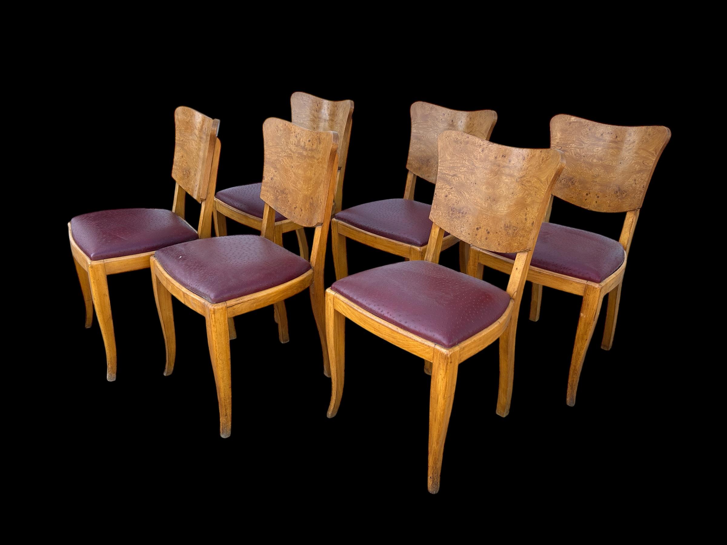 Un refinado juego de seis sillas de comedor francesas de los años 30, fabricadas en una llamativa madera burlada que muestra una veta bellamente labrada y una cálida profundidad tonal. Cada silla tiene un respaldo de formas elegantes y líneas art