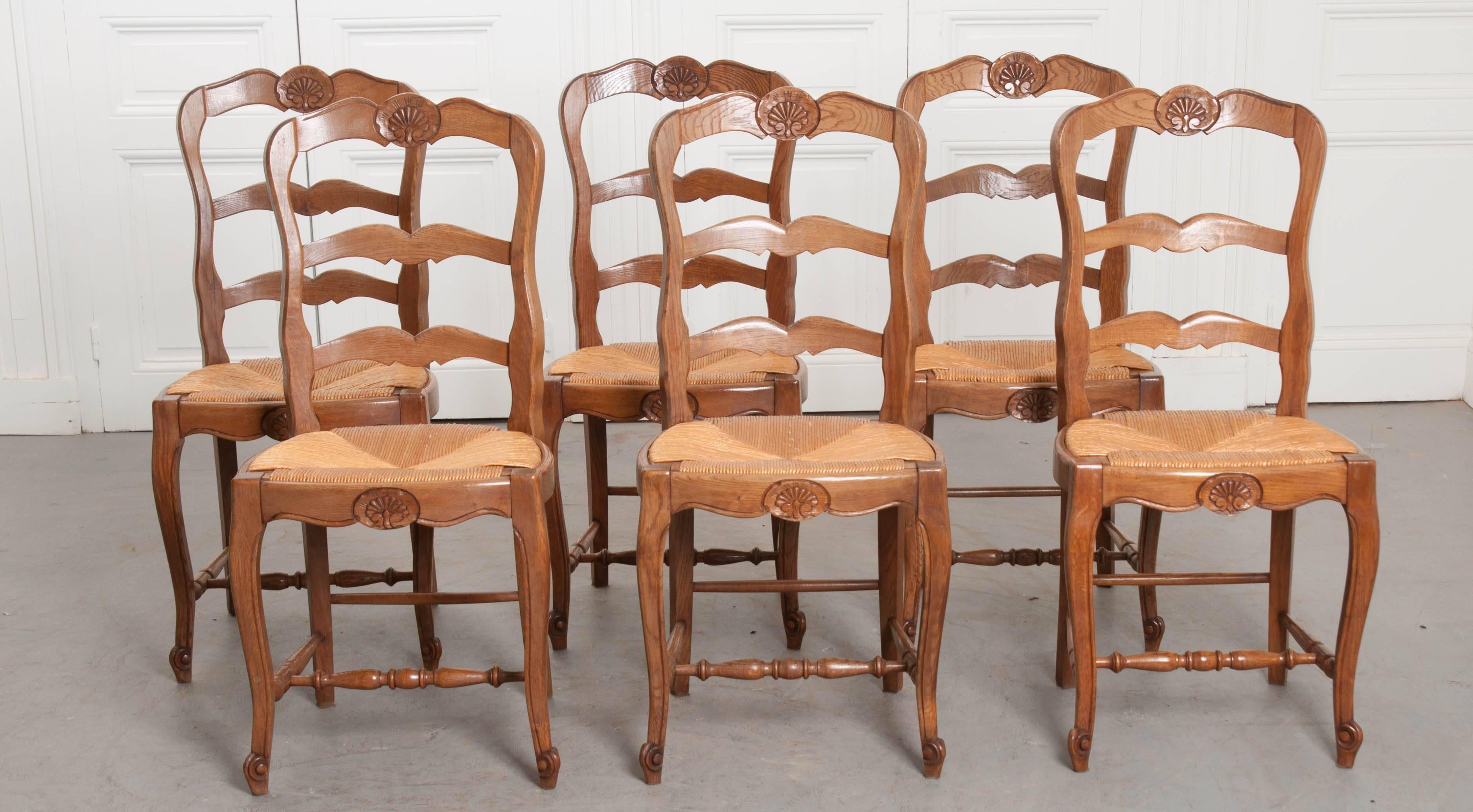 A charming set of six French oak ladder back chairs made in the 1940s. A beautiful carved shell cartouche graces the chairs’ top and front rails. The rush seats are in excellent antique condition and have a height of 18 1/2. The seats are removable.