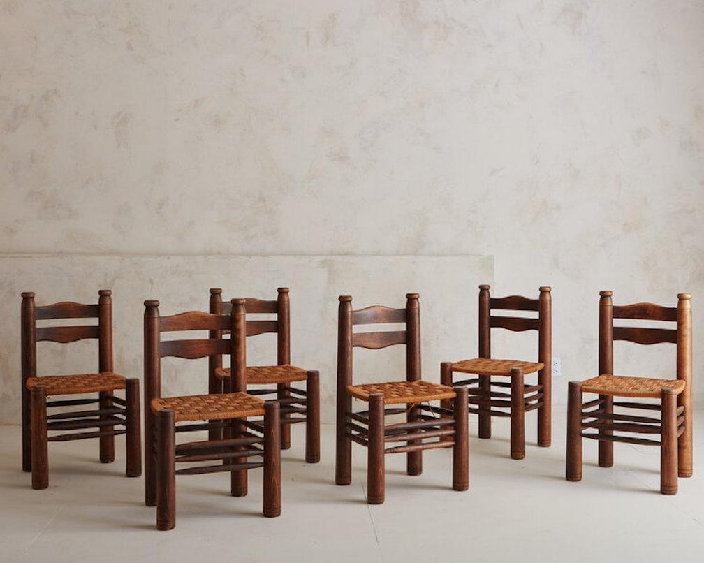 A set of six ladder-back carved beech wood dining chairs with rush seats featuring a woven rush seat. These chairs are in the style of the early 20th-Century French designer, Charles Dudouyt. France, 1940s.