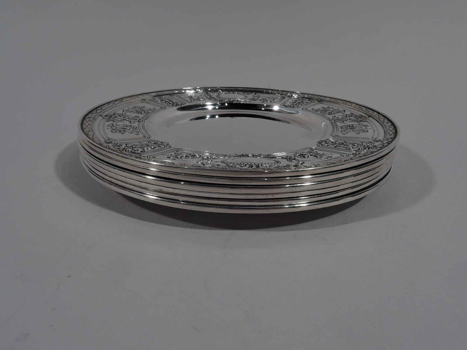Set of 6 sterling silver bread and butter plates in Maintenon. Made by Gorham in Providence in 1928. Each: Deep and plain well. Wide shoulder with chased leafy-scrollwork and flowers spilling over curvilinear frames. Two beaded oval frames (vacant).