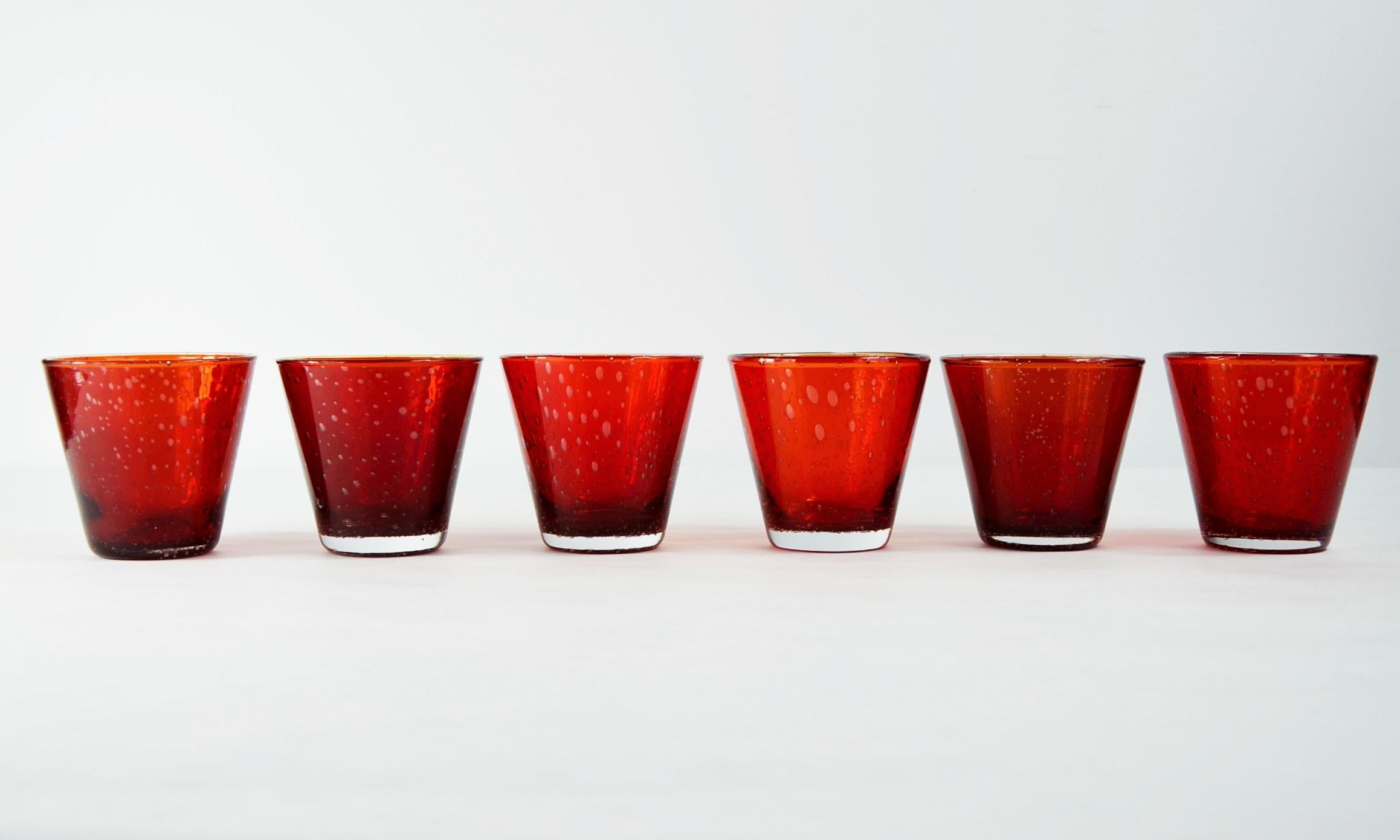 Offered is a set of six Mid-Century Modern Italian Murano tapered cocktail glasses featuring a beautiful ruby red glass cased in clear glass with gas controlled bubble decoration. Look closely into the bubbles and slowly turn the glass around and
