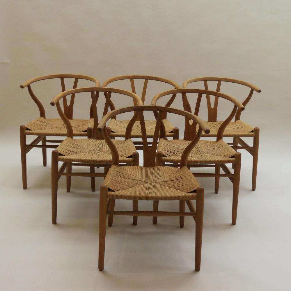 A wonderful set of early edition Wishbone Chairs, Model number CH24. Designed by Hans J Wegner and manufactured by Carl Hansen, this set was produced in the 1960s. Made from solid Oak with original papercord seats. In excellent condition. A set of 6