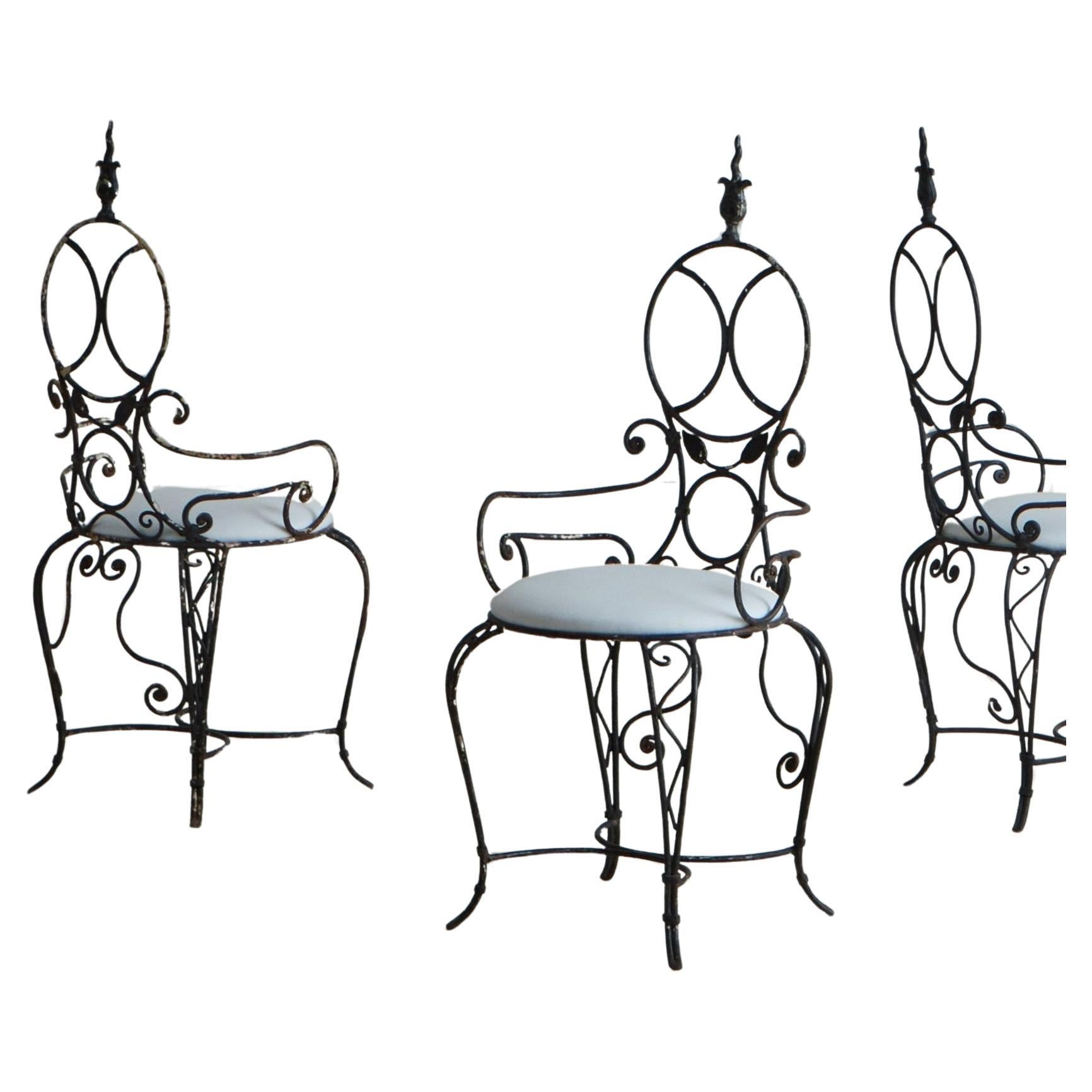 A set of 6 vintage French dining chairs featuring intricate wrought iron frames with elegant scrolls, leaf motifs and an X-support bar. These chairs have circular seatbacks with decorative finials and stand on curved, cabriole legs. The circular