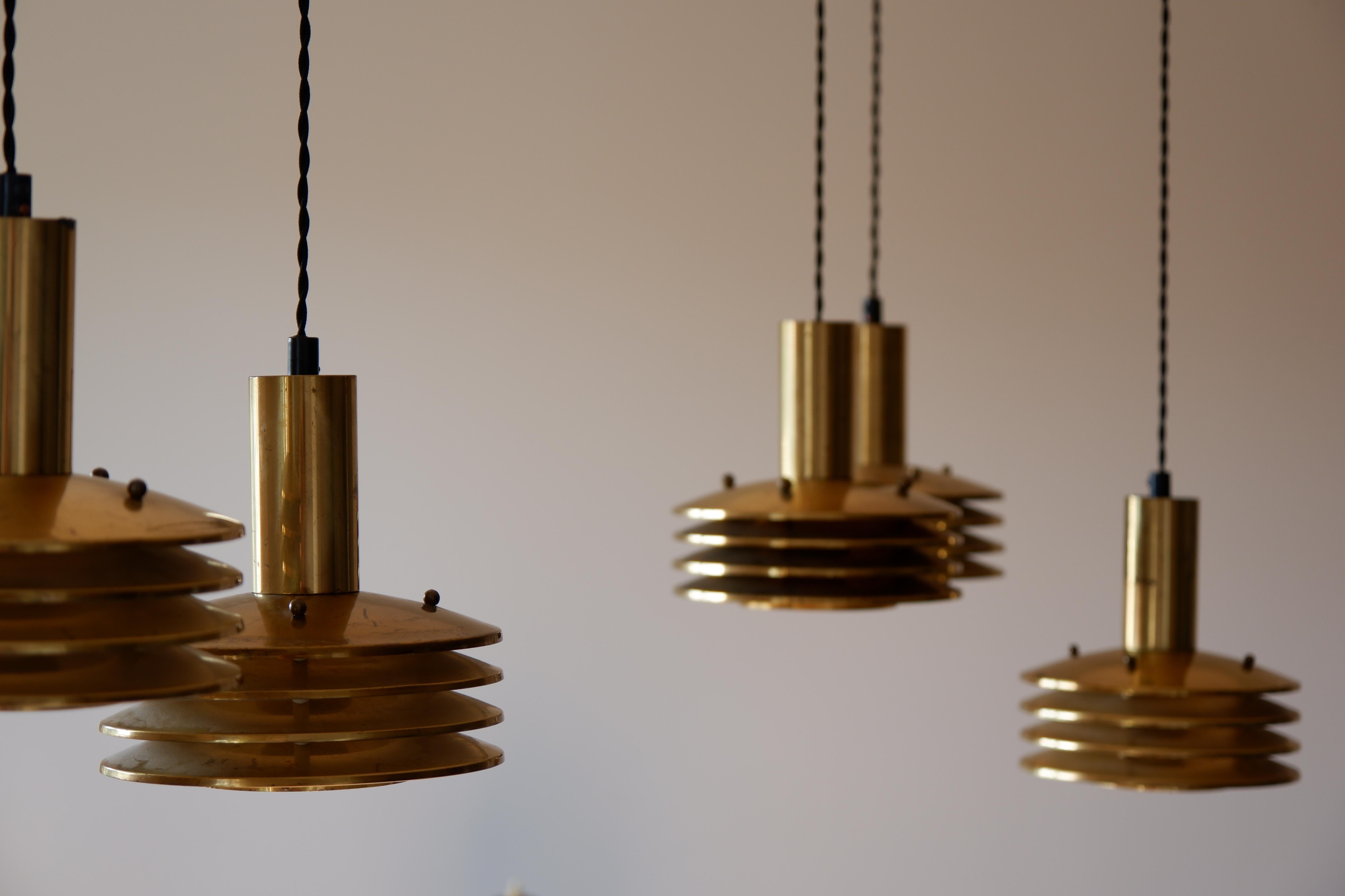 Rare set of 6 Kai Ruokonen lamps, made in solid brass with 4 rings and a glass diffuser. The lamp is composed by two set of 3 lamps hold by a ceiling cup distributors. The overhall condition is good and each lamp has a good patina with trace of use