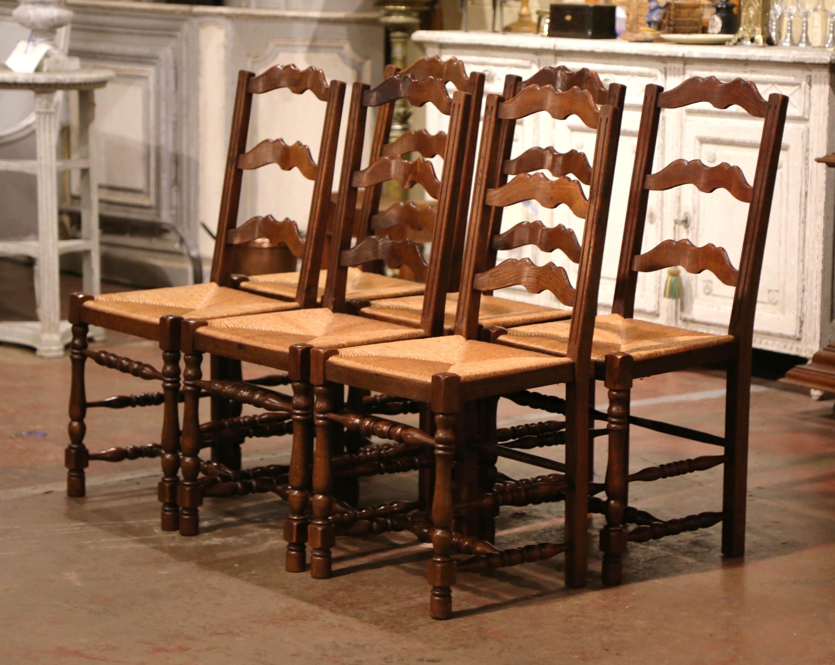 These six elegant country chairs were crafted in Normandy, France, circa 1960. Carved from solid oak, each chair stands on carved turned legs embellished with a bottom stretcher. Each chair has a tall pitched back with three scalloped ladders across