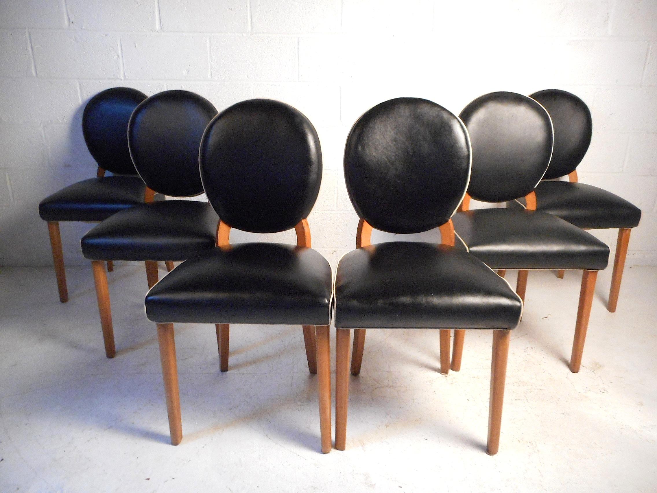 This unique set of dining chairs feature black faux-leather upholstery which is lined with white trim giving the chairs an interesting visual profile. The upholstery is secured by tufts on the backside of the chairs. Sturdy wooden frame supports. A