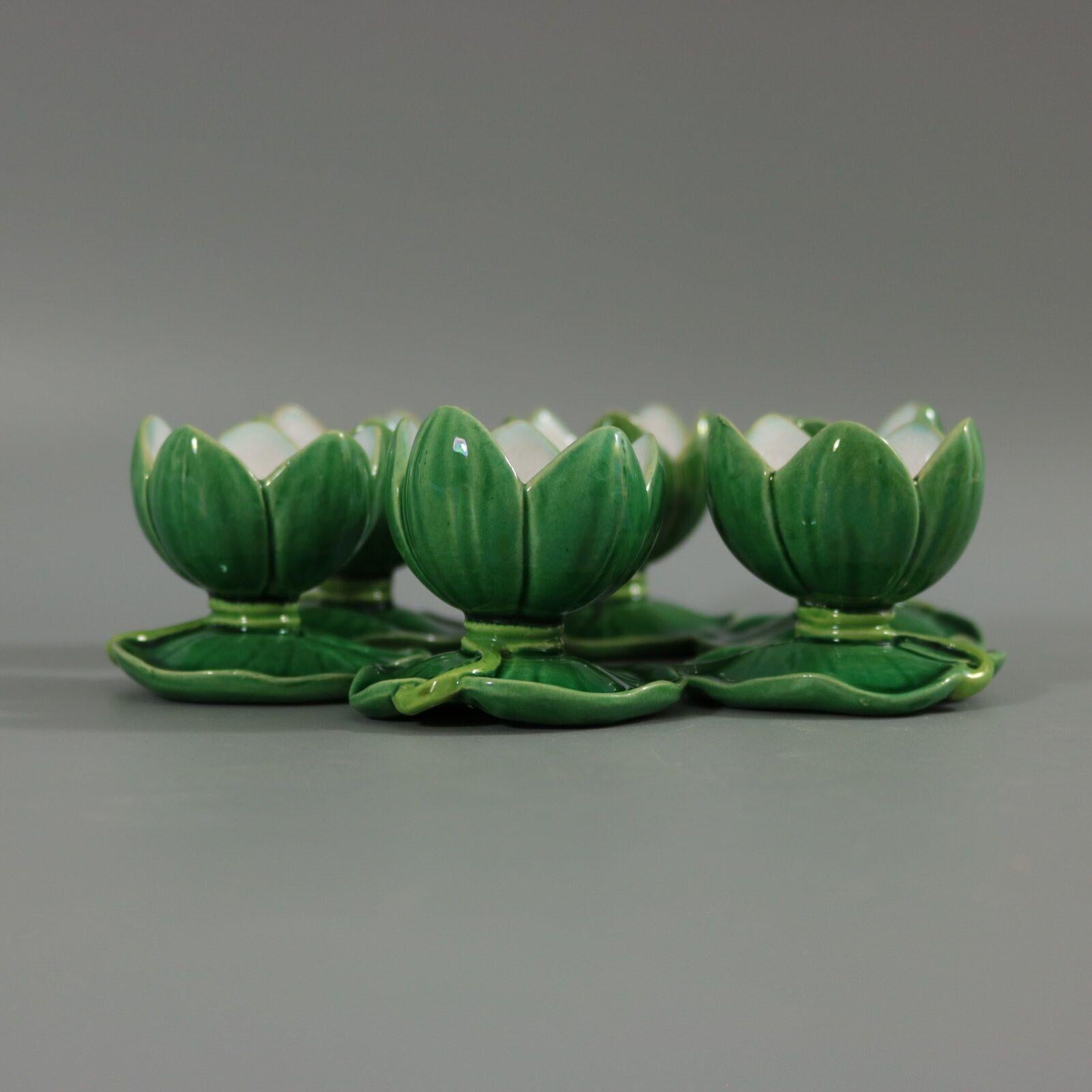 Set of three Minton Majolica egg cup holders which feature a lily pad base with lily flower egg receptacles. Colouration: green and white are predominant.