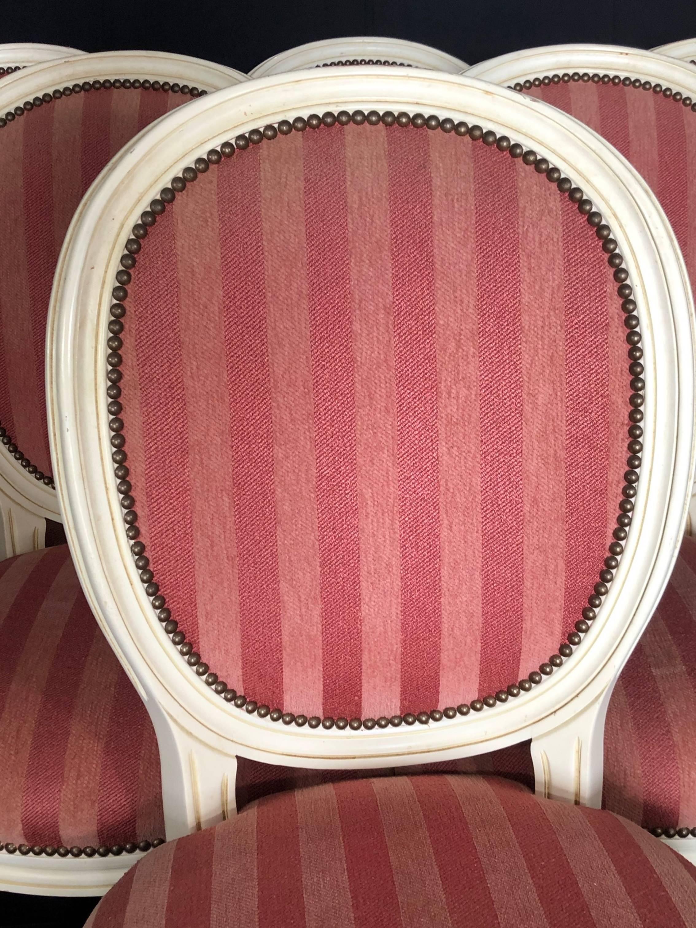 A set of six pretty painted French Louis XVI style dining chairs with elegant cameo backs and turned tapering fluted legs. The elegant upholstery is raspberry stripe on the front with nailhead detailing, and complementary plaid fabric on the backs.