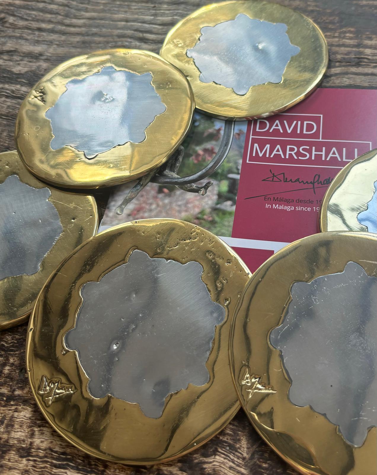 The round coasters  were created by David Marshall, from sand cast aluminium.
 We use recycled materials all our pieces are handmade, mounted and finished in our foundry and workshop in Spain.
It is certified authentic by the Artist David