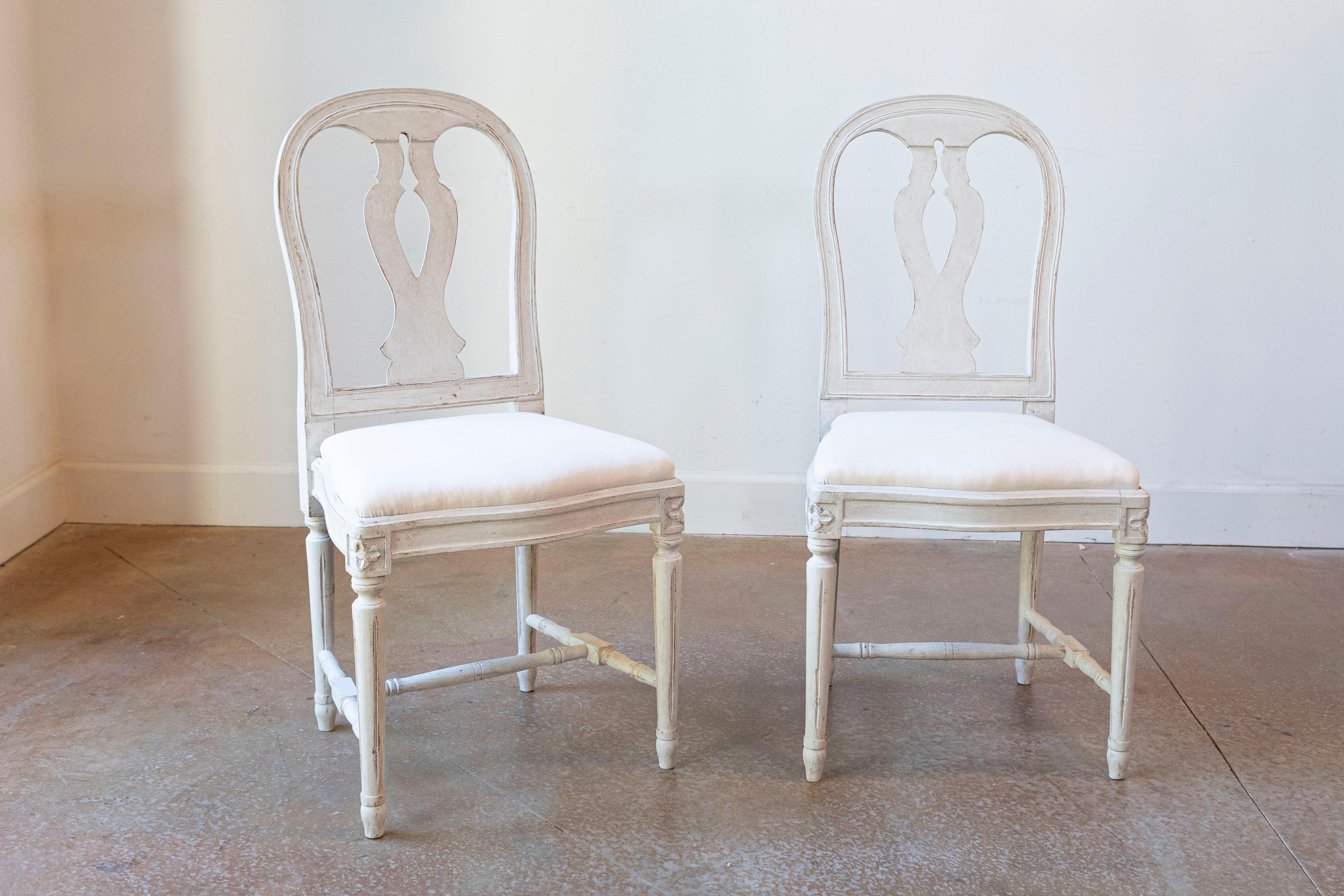 Ensemble de 6 chaises de salle à manger suédoises en bois peint du début du 20e siècle, avec des éclisses sculptées, des pieds cannelés et une nouvelle tapisserie blanche. Créée en Suède au début du siècle, cette série de 6 chaises d'appoint se