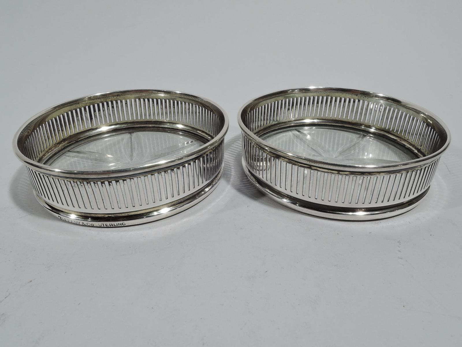 Set of 6 Modern sterling silver and glass coasters, ca 1920. Retailed by Tiffany & Co. in New York. Each: Round clear glass well with cut stylized flower. Sterling silver gallery with linear piercing. Marked “Tiffany & Co. Sterling”.