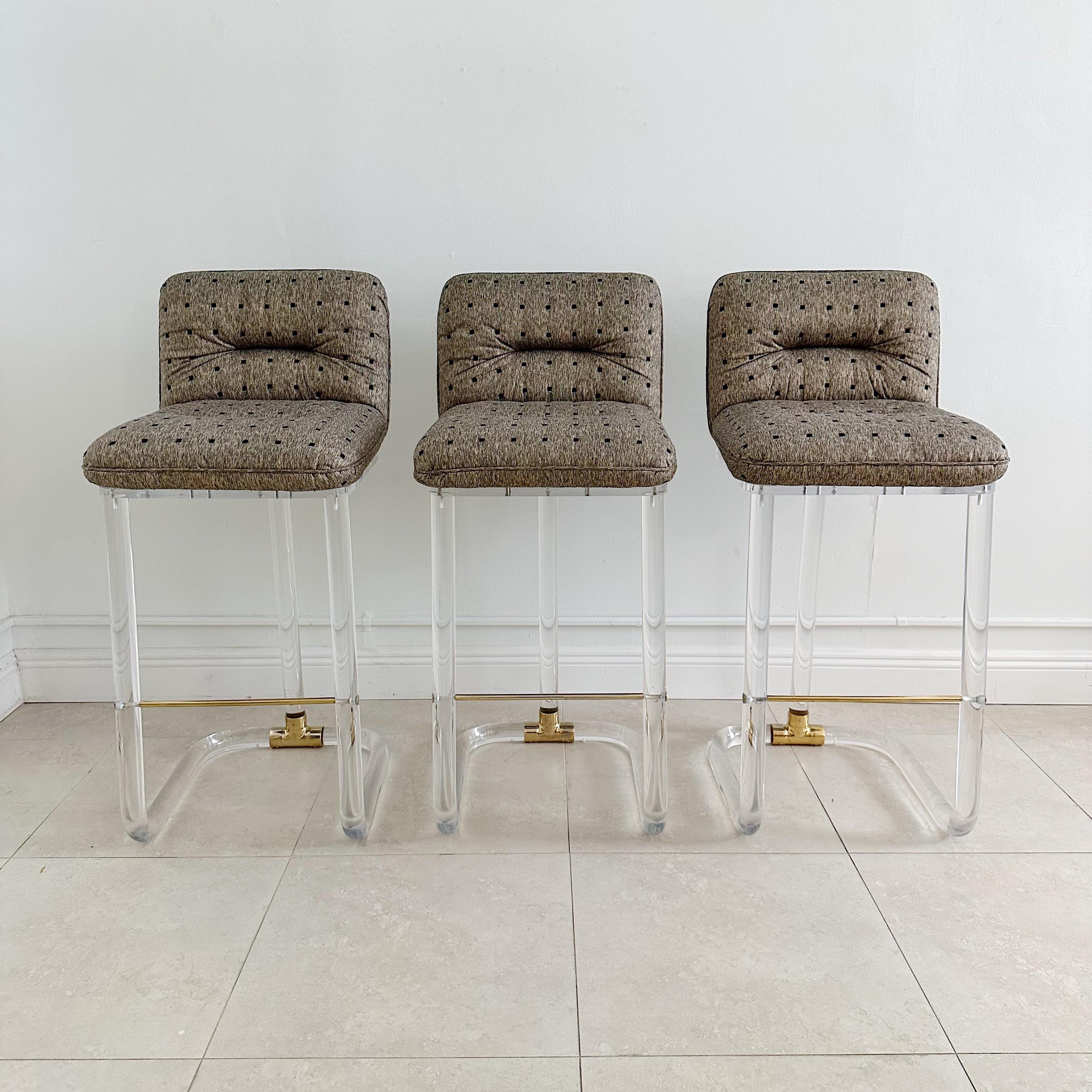 Set of six lucite and brass swivel bar stools by Leon Frost for Lion in Frost, circa 1970s. Featuring a curved tubular lucite bar frame, the seats still have the original upholstery which is in excellent condition. The stools are adorned with brass
