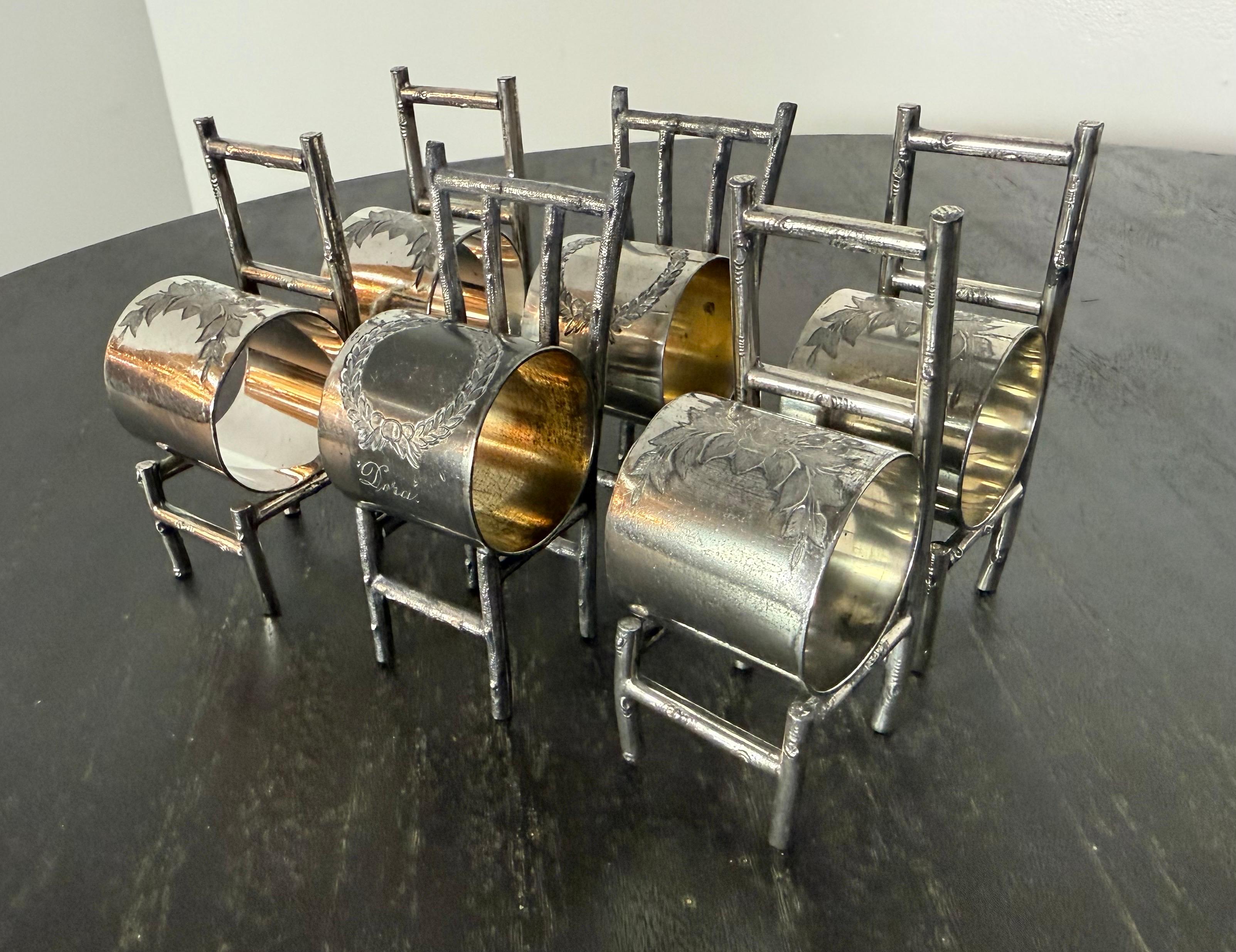 This charming and whimsical set of six antique silver-plated napkin ring holders is cleverly crafted in the form of miniature chairs. Four of the holders share one distinct style, while the remaining two are in a slightly different design, making