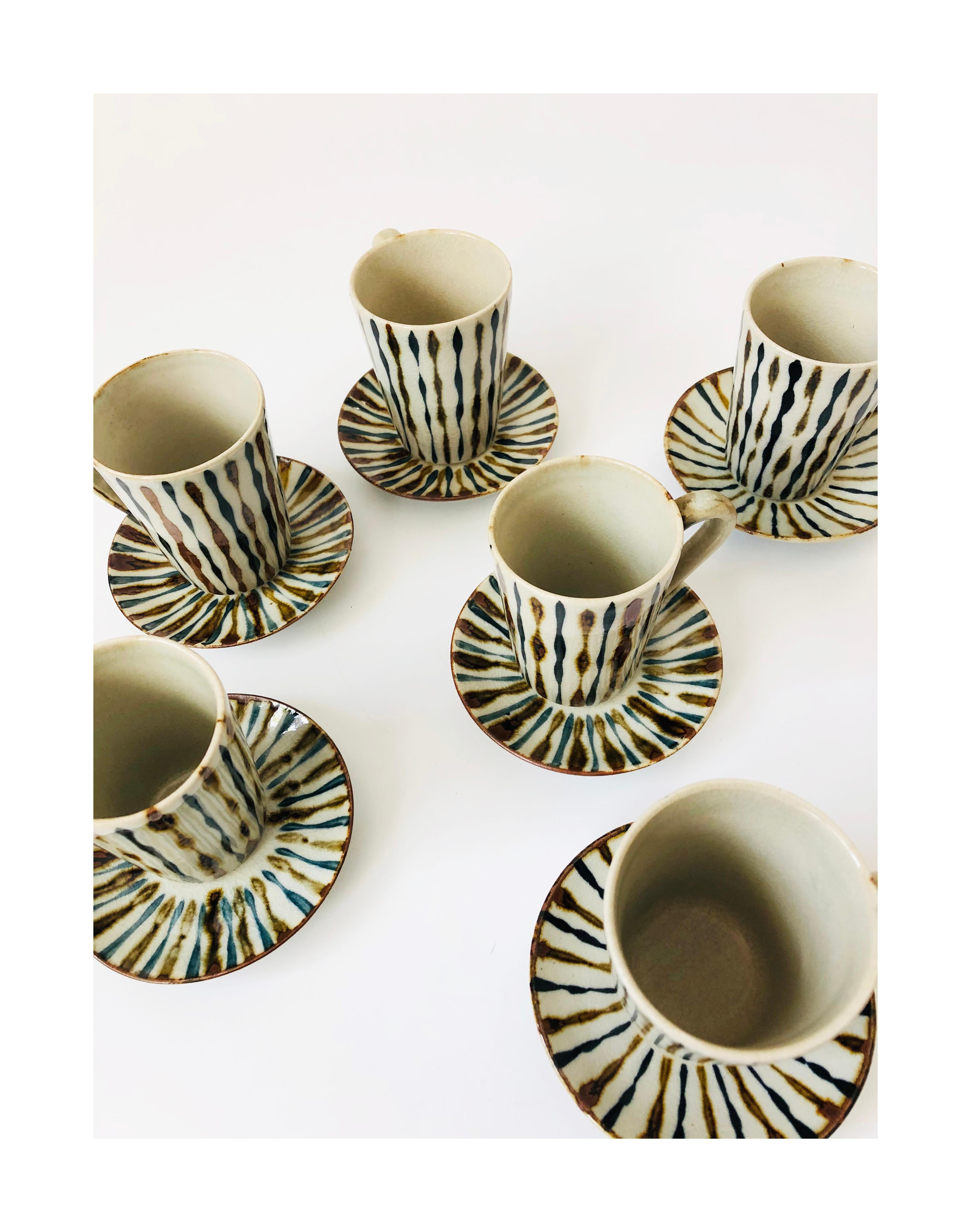 A set of 6 vintage handmade pottery demitasse mugs and saucers. Each piece is decorated with a painted dark blue and brown striped design over a gray base color.
Each mug measures 3.25