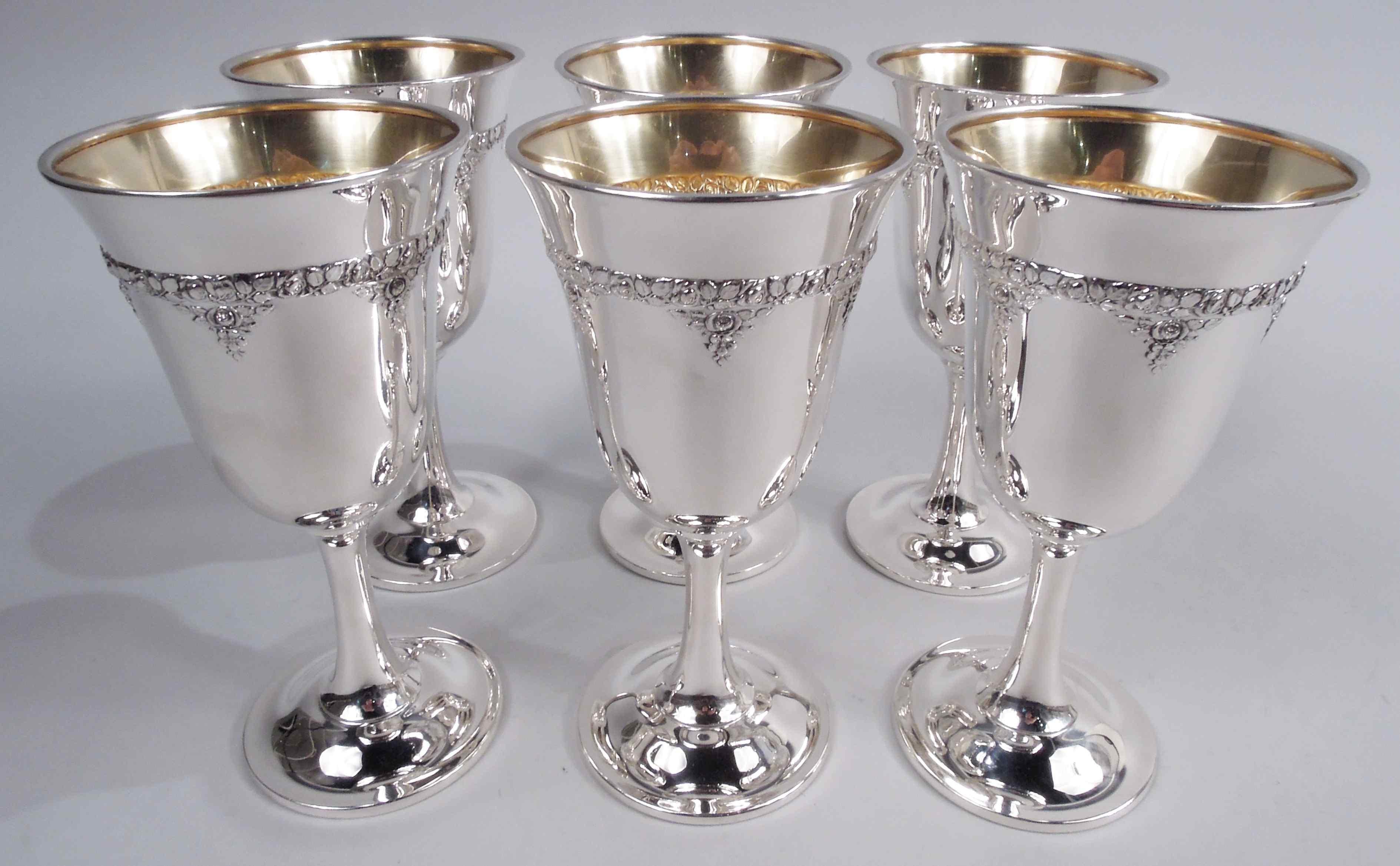 Six Normandie sterling silver goblets. Made by Wallace in Wallingford, Conn. Each: Tapering bowl with curved bottom; cylindrical stem on gently raised foot. Dense floral border with pendants. Bowl interior gilt. A nice set in a fresh and pretty