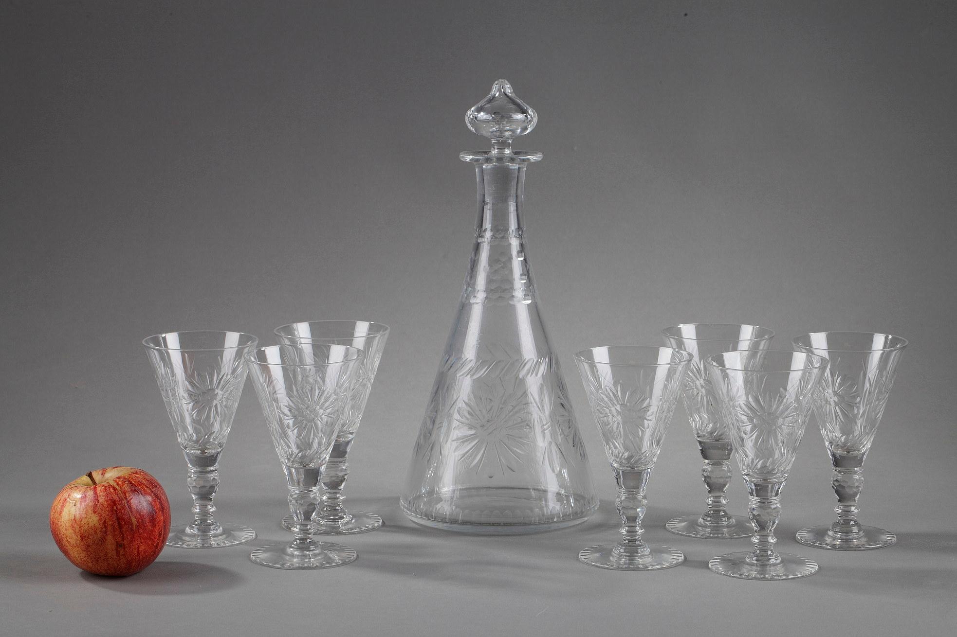 Decanter and seven crystal liqueur glasses decorated with cut flowers and friezes of pearls. The glasses in the shape of an inverted pyramid rest on a foot decorated with a faceted sphere. The foot is cut with decorative lines. The carafe of conical