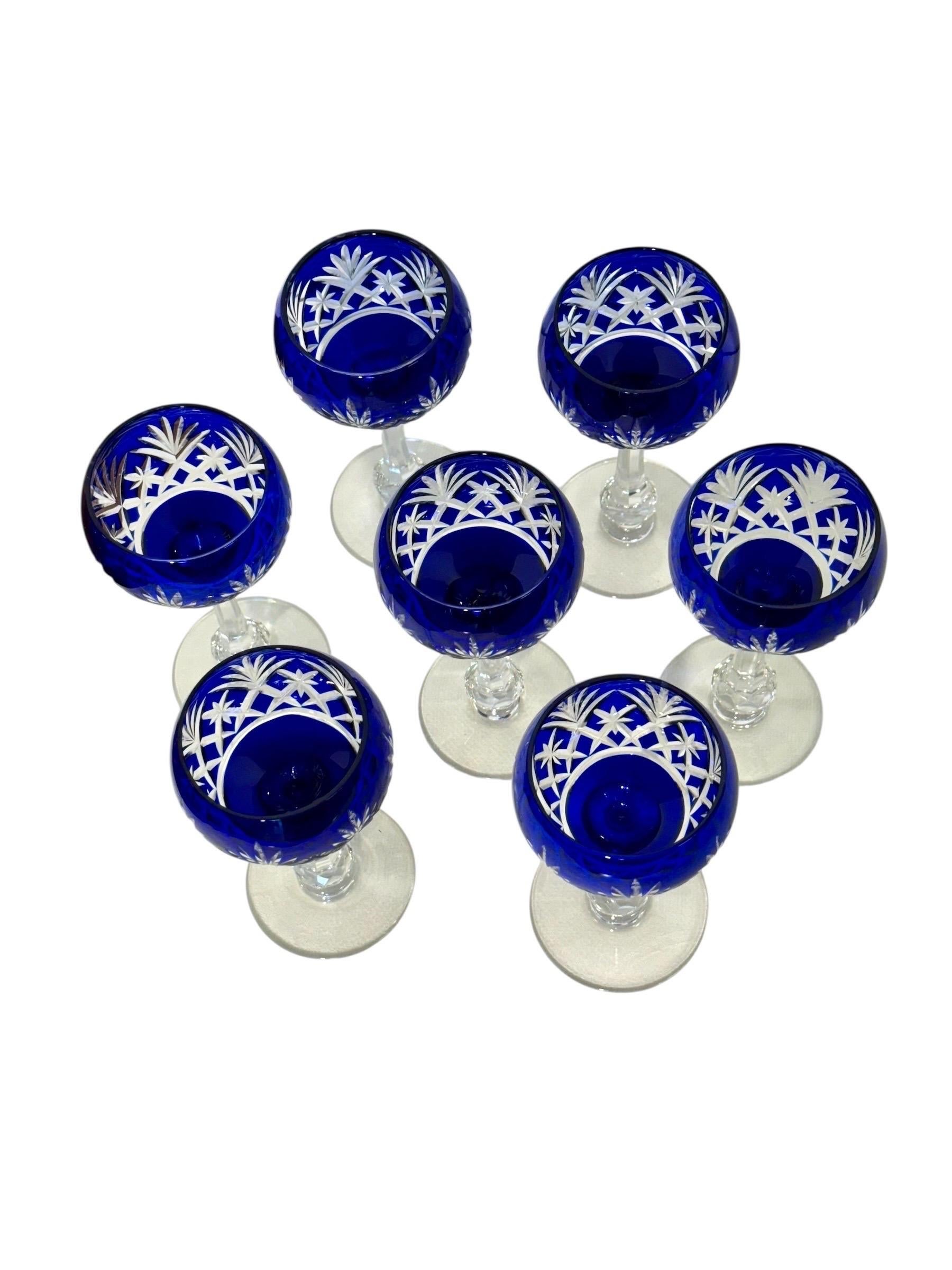 Cet élégant ensemble de sept verres à pied en cristal est réalisé en overlay bleu cobalt profond, taillé en clair, et conçu dans le style raffiné de Saint-Louis, l'une des plus prestigieuses manufactures de cristal françaises. Chaque verre présente