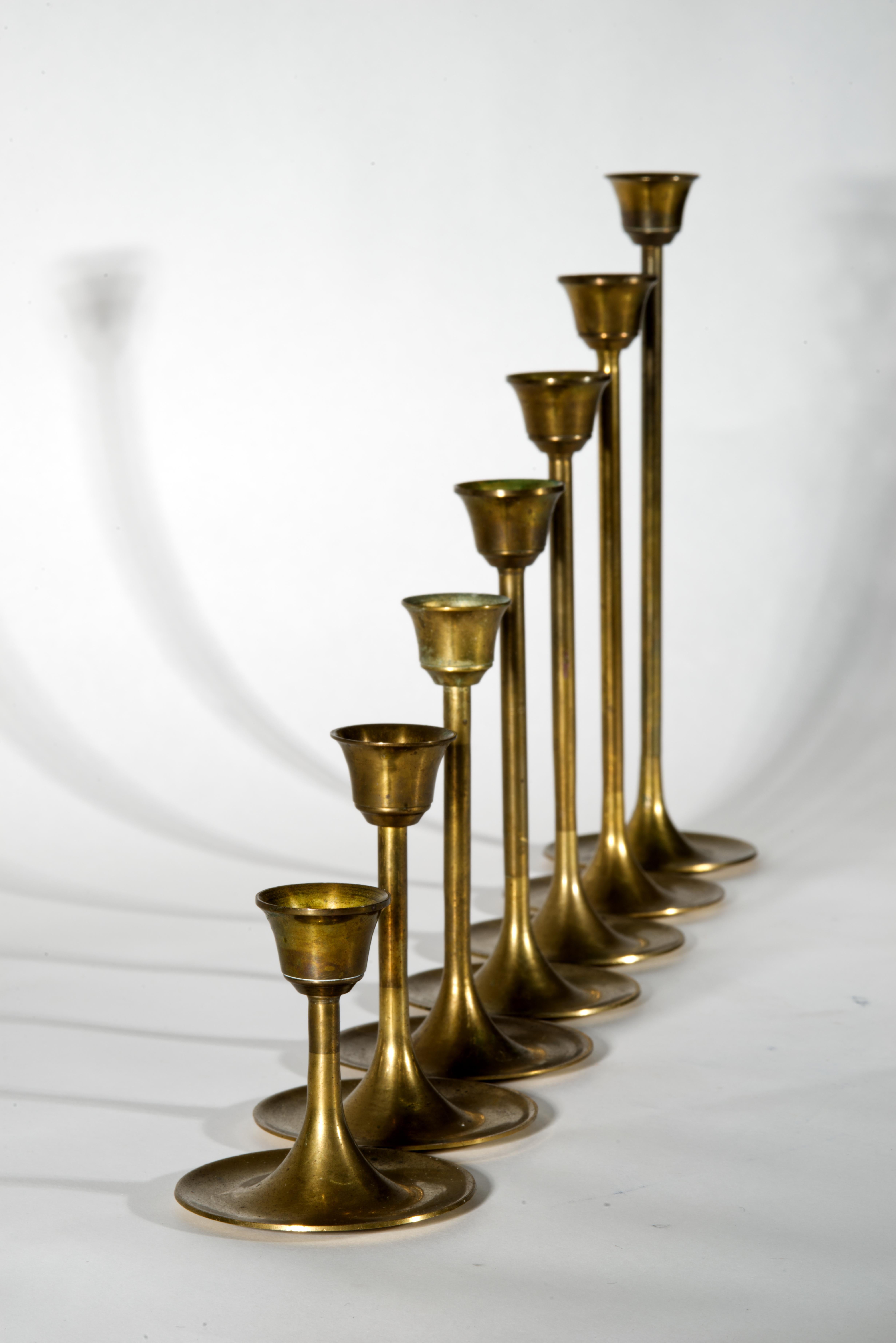 Set of 7 vintage brass candle holders in Scandinavian Modern style features elegant, slender forms with round flared bases and tulip shaped sconces. Warm, golden color, soft sheen, and tactile quality of solid brass complements minimalist, Bauhaus