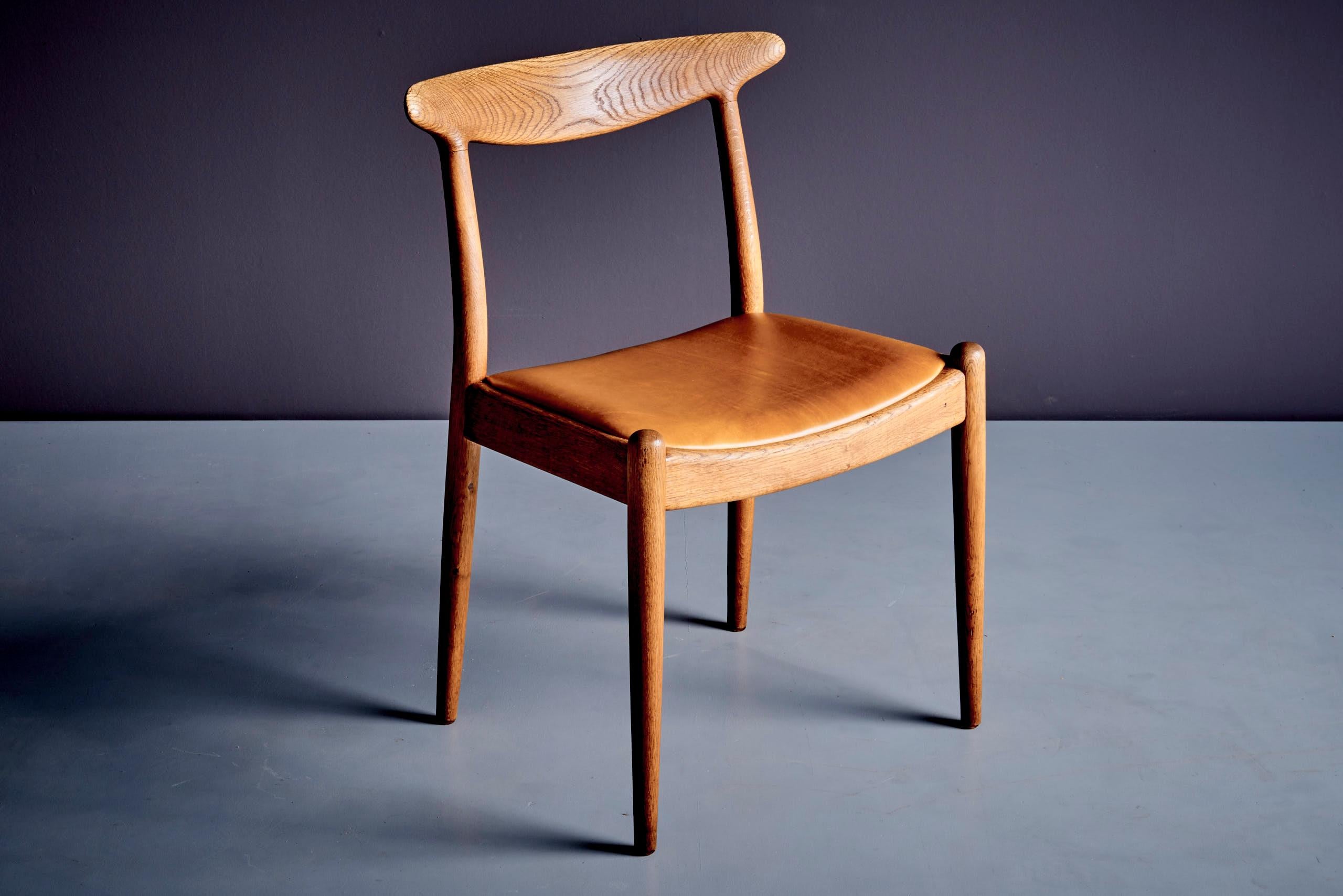 A set of 7 'W2' chairs, designed by Hans J. Wegner in Denmark during the 1960s. These oak-framed chairs showcase a sleek, modern design, highlighted by beautifully sculpted backrests and the rich, warm tones of the oak wood. These chairs exemplify