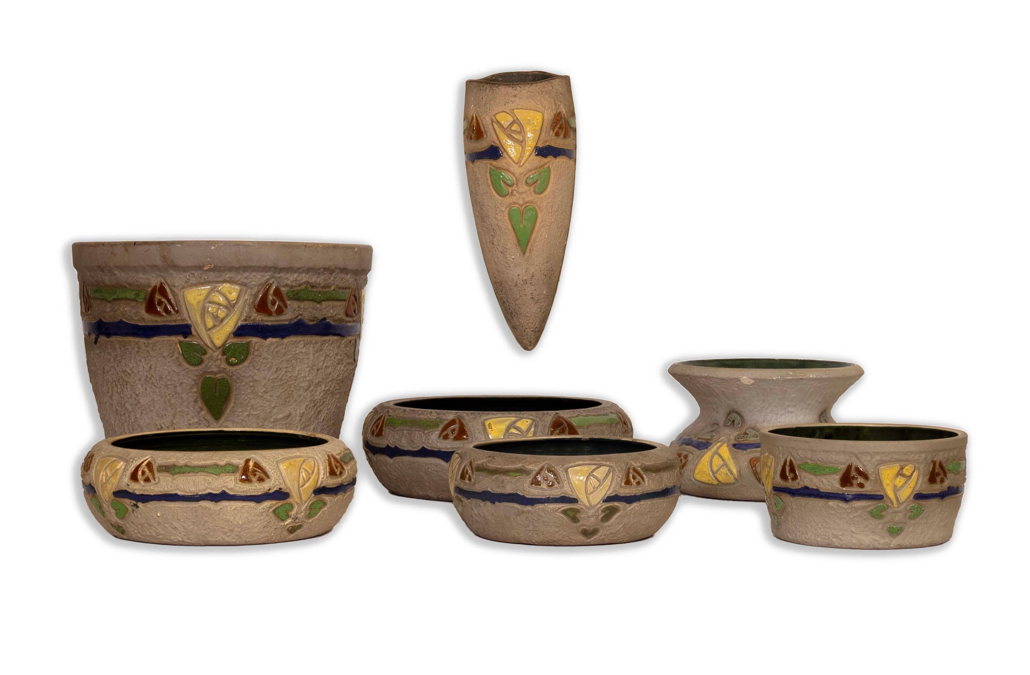 Vibrant and exquisite, this Set of 7 Roseville Ceramic Pottery Pieces from the early 20th century is a stunning example of Arts and Crafts design. Each piece features intricate, colorful motifs in yellow, green, and blue against a textured backdrop,
