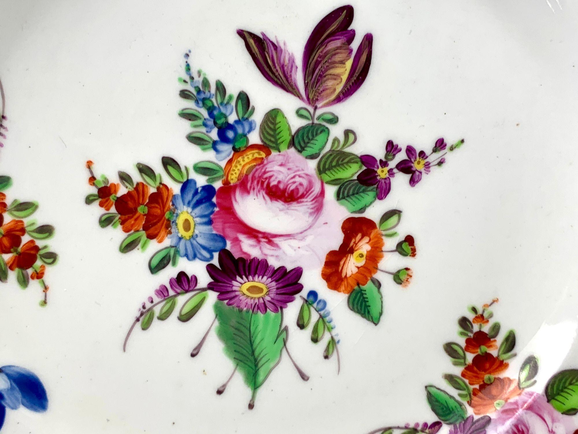 Cet ensemble de huit assiettes anciennes en porcelaine anglaise présente une décoration florale vibrante peinte à la main.
Fabriquée à Derby vers 1825, chaque assiette présente un bouquet exubérant de fleurs de jardin, dont des roses, des tulipes et