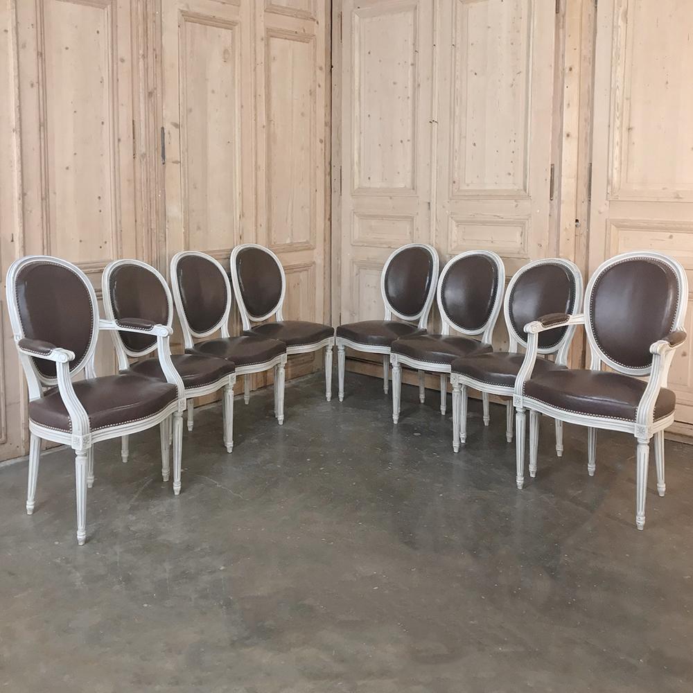 Set of 8 antique French Louis XVI dining chairs includes 2 armchairs feature an original white painted finish and real leather upholstery on the back and seats for elegant entertaining in style. Oval neoclassical seat-backs are contoured for comfort