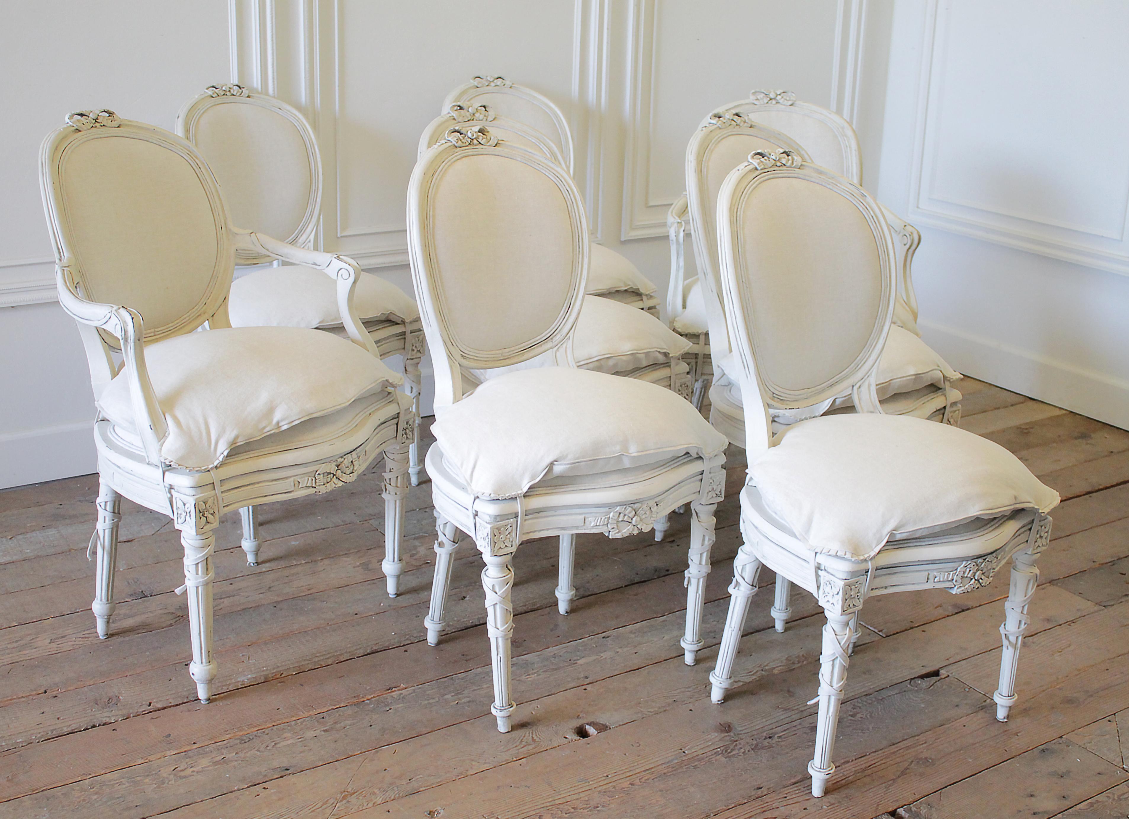 Set of 8 antique Louis XVI style painted and upholstered dining chairs with slip covered seat cushions. Beautiful carved ribbons, and fluted legs. We have painted these in a soft oyster white finish, with subtle distressed edges, and finished with