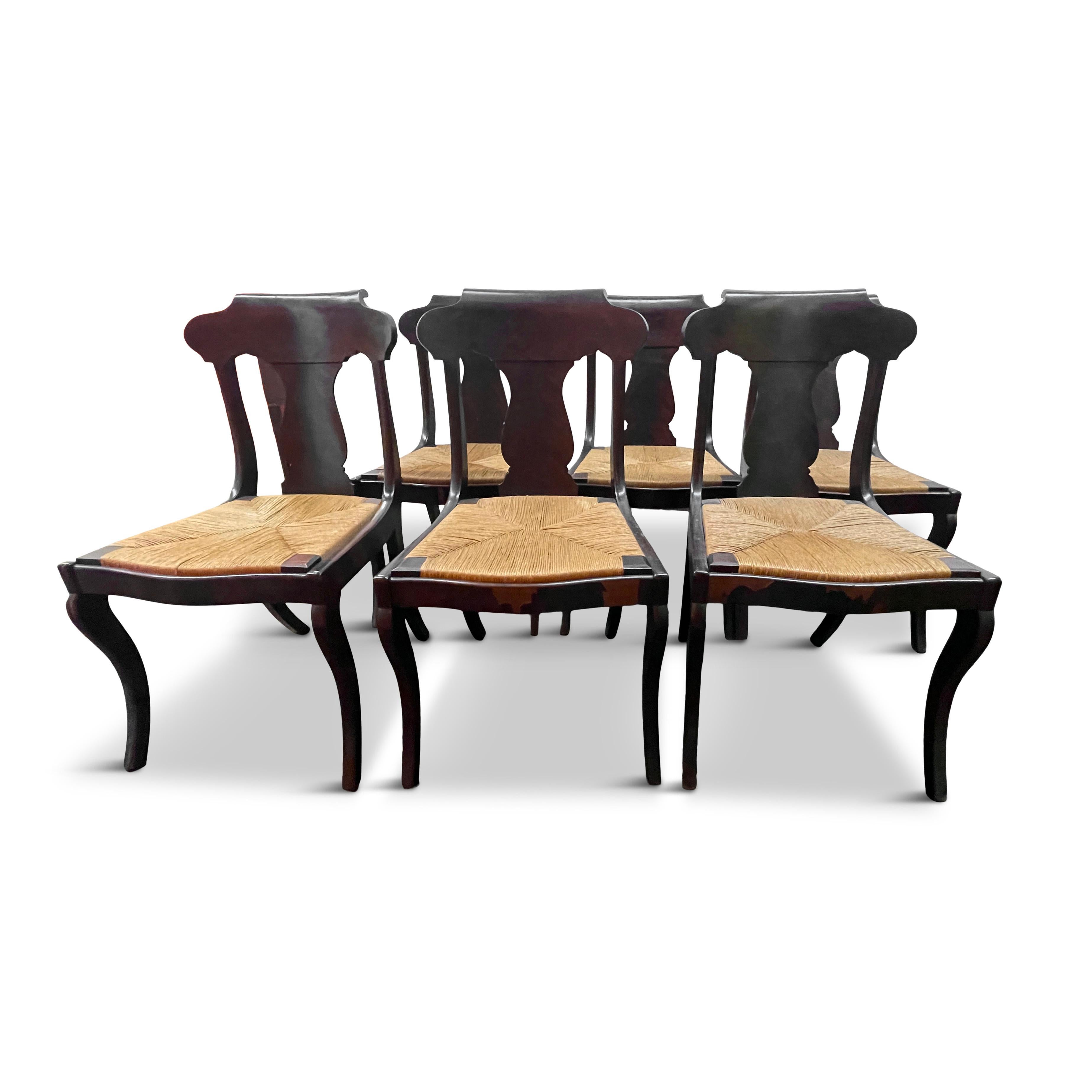 A lovely set of eight chairs with arched back, urn shaped back plate, saber front legs, splayed back legs, mahogany veneer over hardwood, and woven rush seats. From the mid to late 19th century, this set of chairs are traditional in materials,