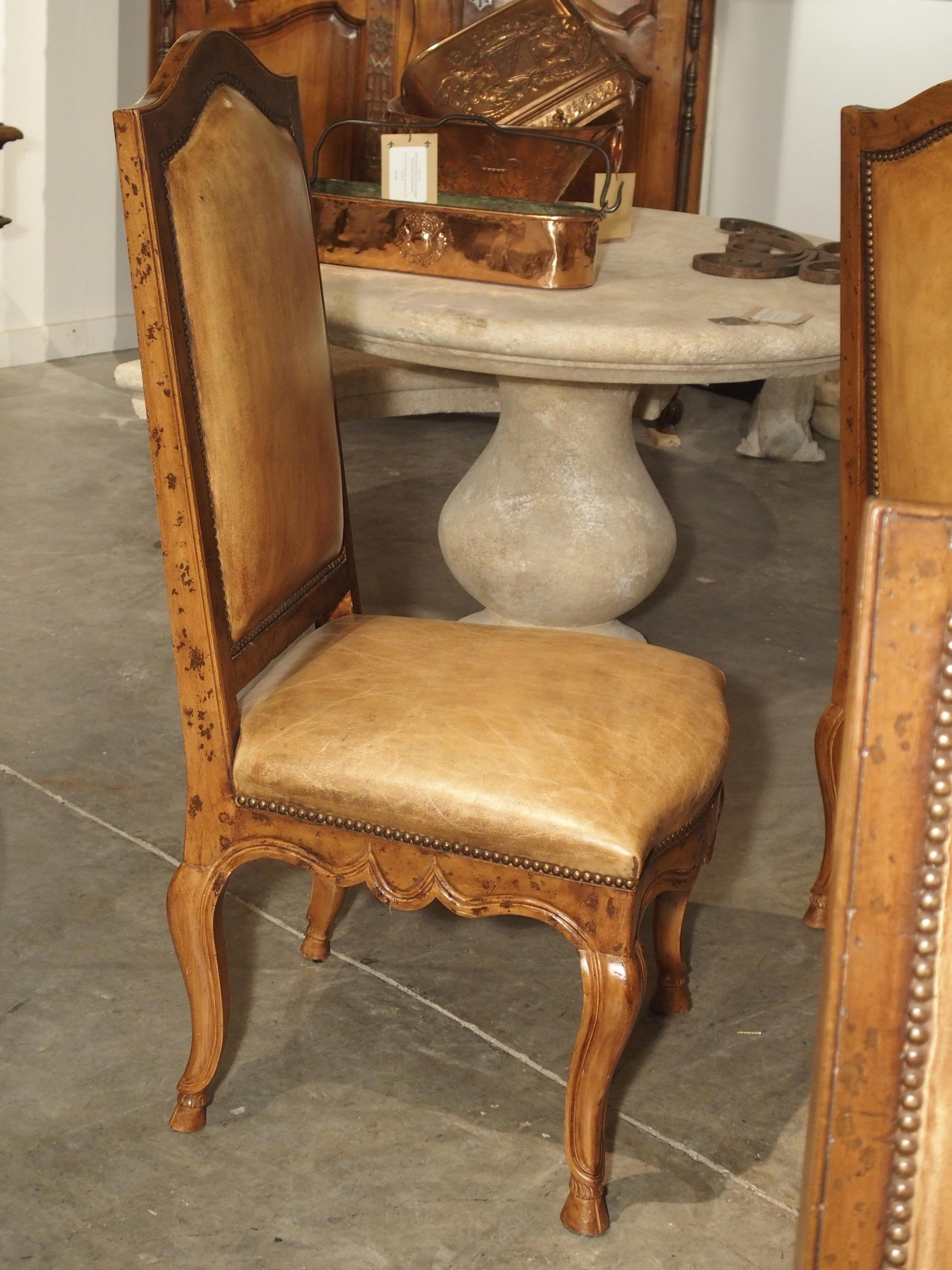 These comfortable and elegant antique Regence style leather and fruitwood chairs have double sided brass nailheads holding the leather onto the chair backs. The tops have a slight dome shape while the S-shaped legs and front rails have conforming