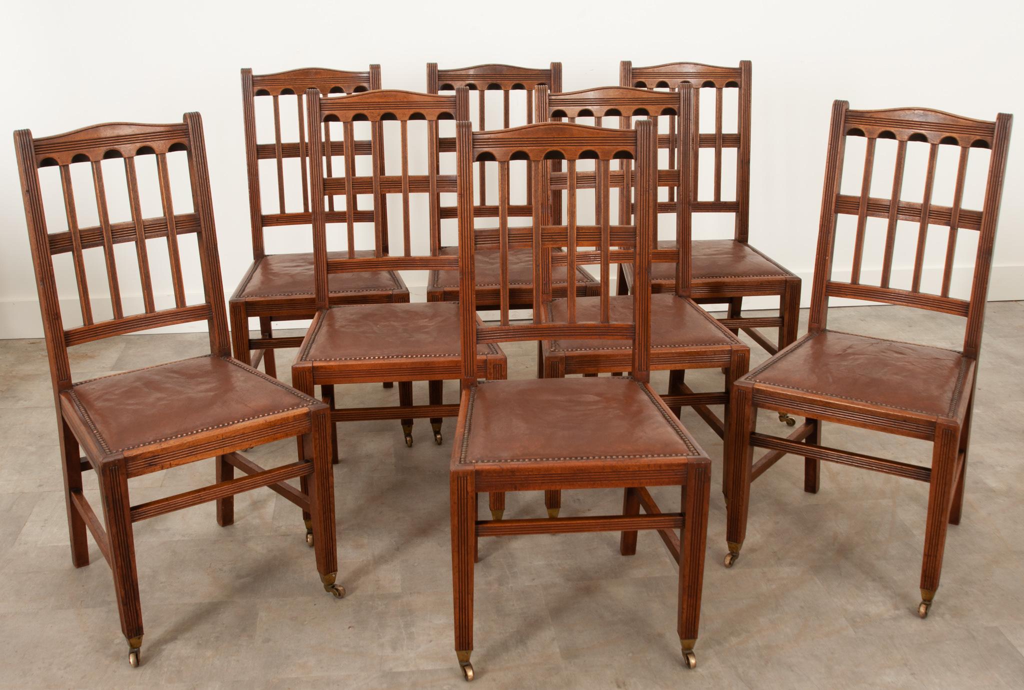 English set of eight arts and crafts dining chairs of impressive design and condition from the 1860’s. The geometric carvings are thoughtfully designed and implemented. Worn leather seats with nailhead trim are comfortable and generous in size. The