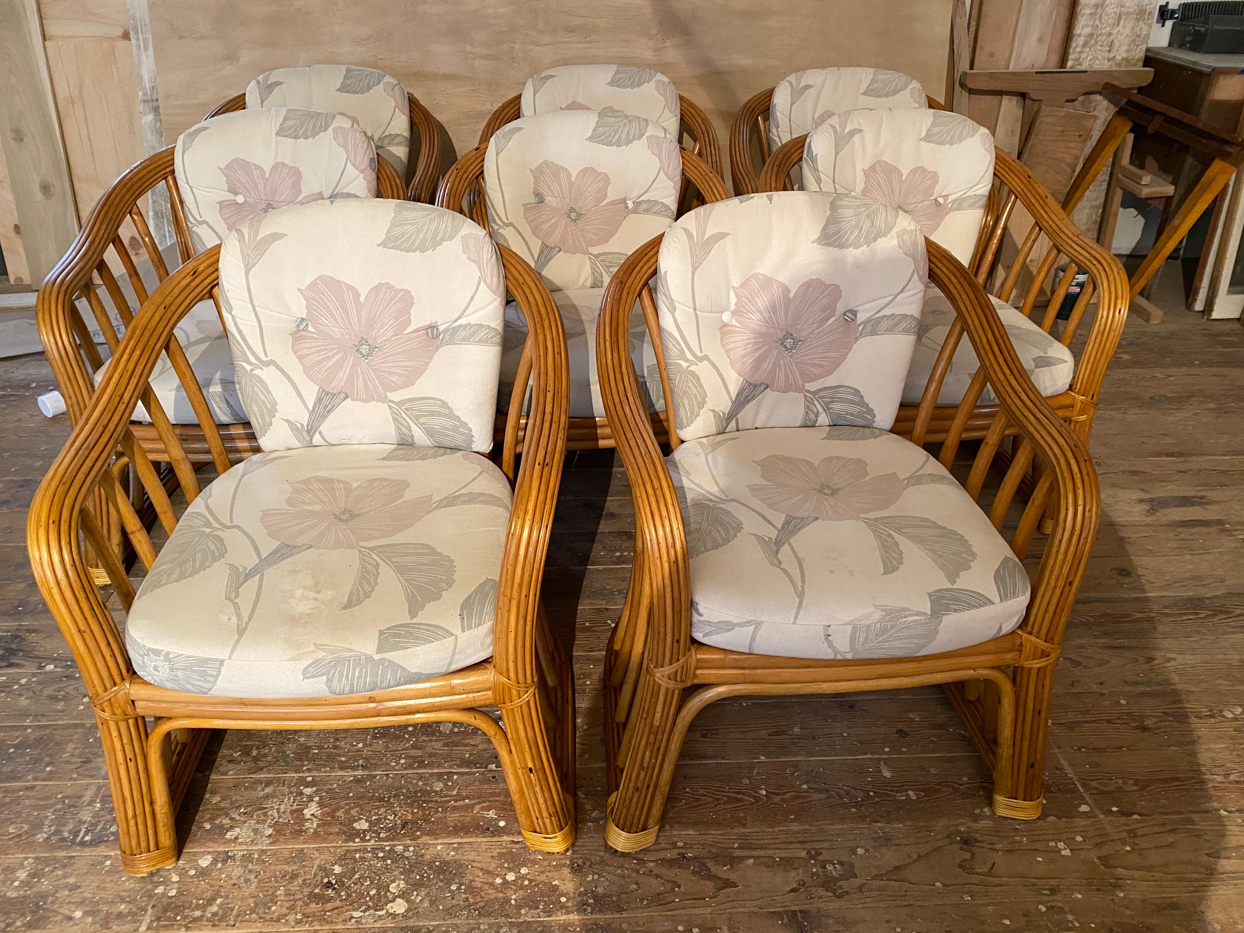 Stylish set of eight bamboo rattan dining armchairs made in the casual California or island coastal style. The backs and arms have gracefully curved shaped. Each chair is topped with a back and seat cushion in a decorative floral motif fabric. These