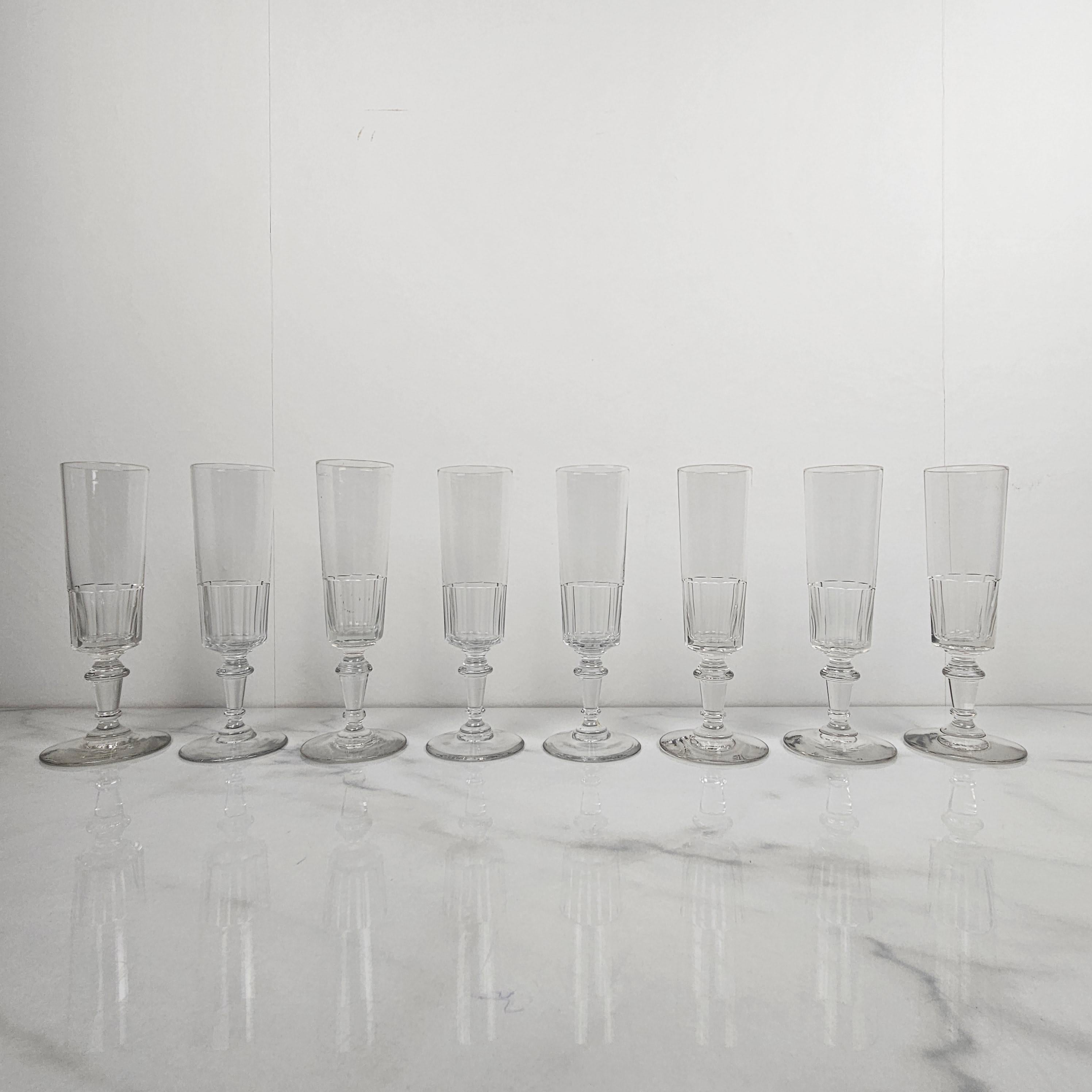 A refined set of eight antique French champagne glasses, crafted from clear glass circa 1880. 
Each flute features a beautifully cut lower bowl and a stem with decorative detailing, offering both visual interest and a graceful silhouette. 
These
