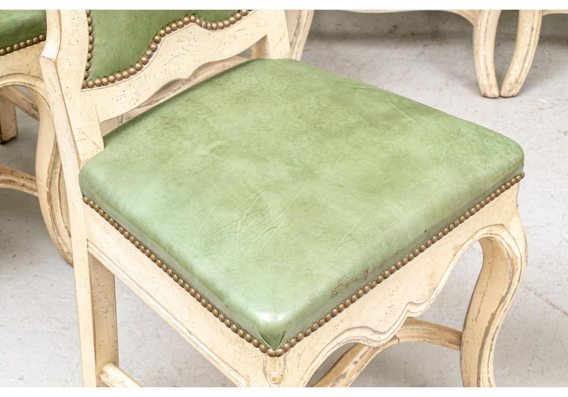 Dramatic Set of 8 high back cream paint decorated dining side chairs with green faux leather upholstery and accented with brass tacks. The crest with a pierced carved shell motif, apron with a deep scalloped form and having a shaped cross stretcher.
