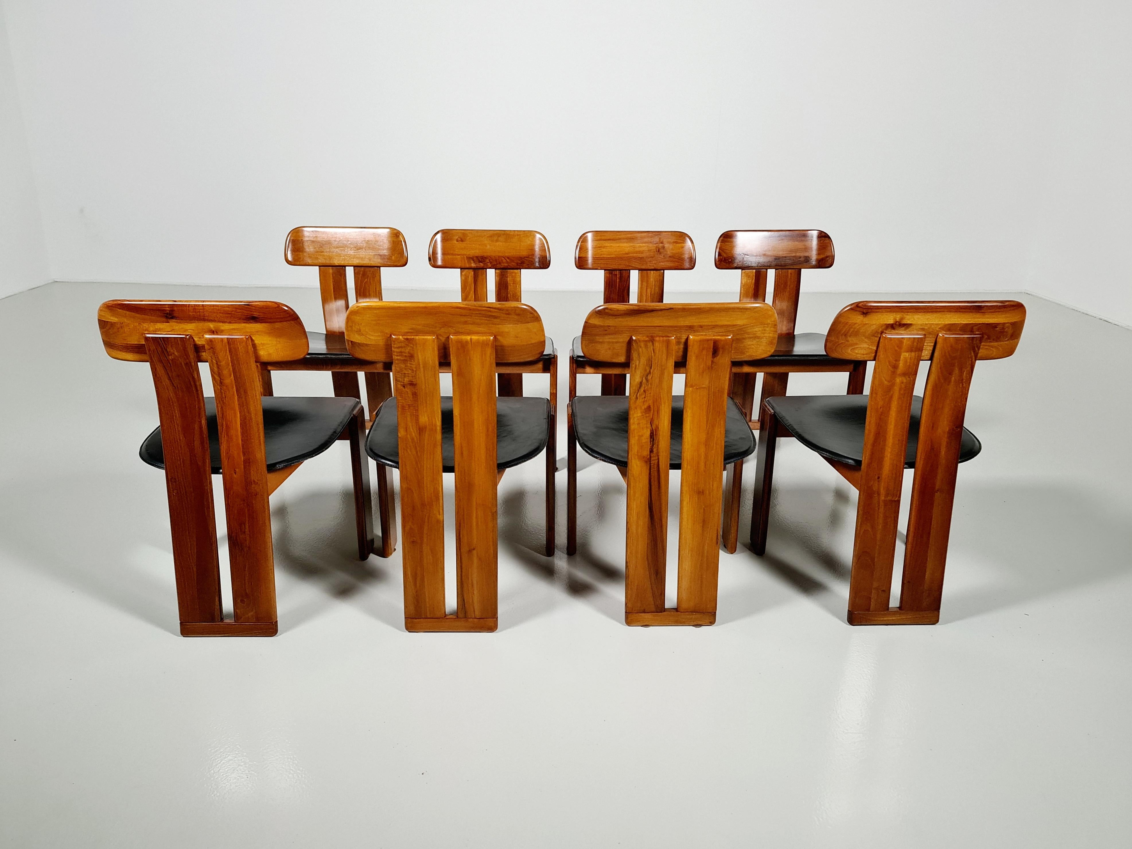 Set of 8 sculptural Italian dining chairs with saddle-stitched leather seats, black colored. Very comfortable even for larger sitters despite the slim profile. The color of the Italian walnut frame is deep and warm which accompanies the patinated