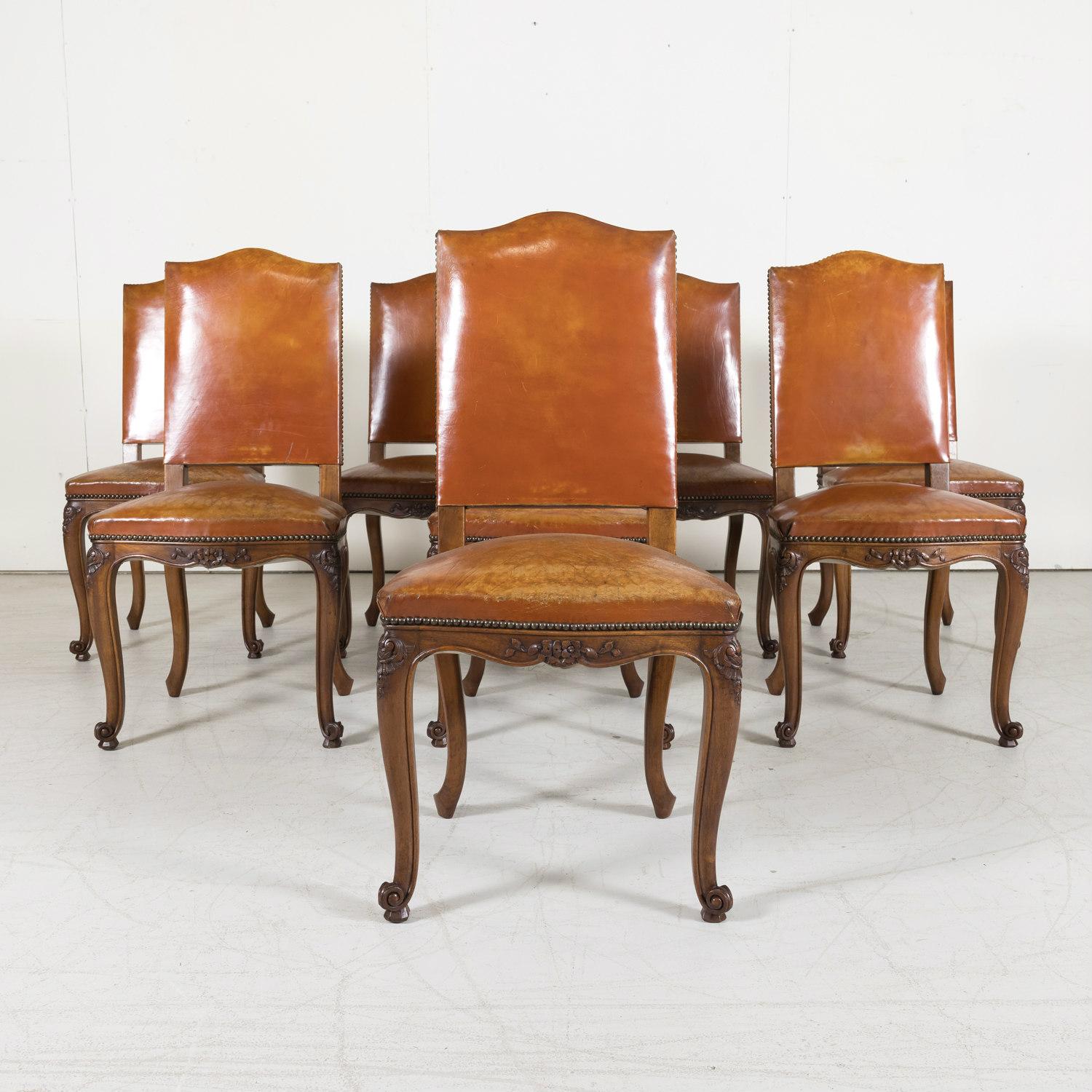 A set of 8 early 20th century French Louis XV style dining side chairs handcrafted in the Loire Valley near Paris, circa 1900, having high slightly slanted chapeau de gendarme backs with cognac color leather upholstery secured with brass nail heads