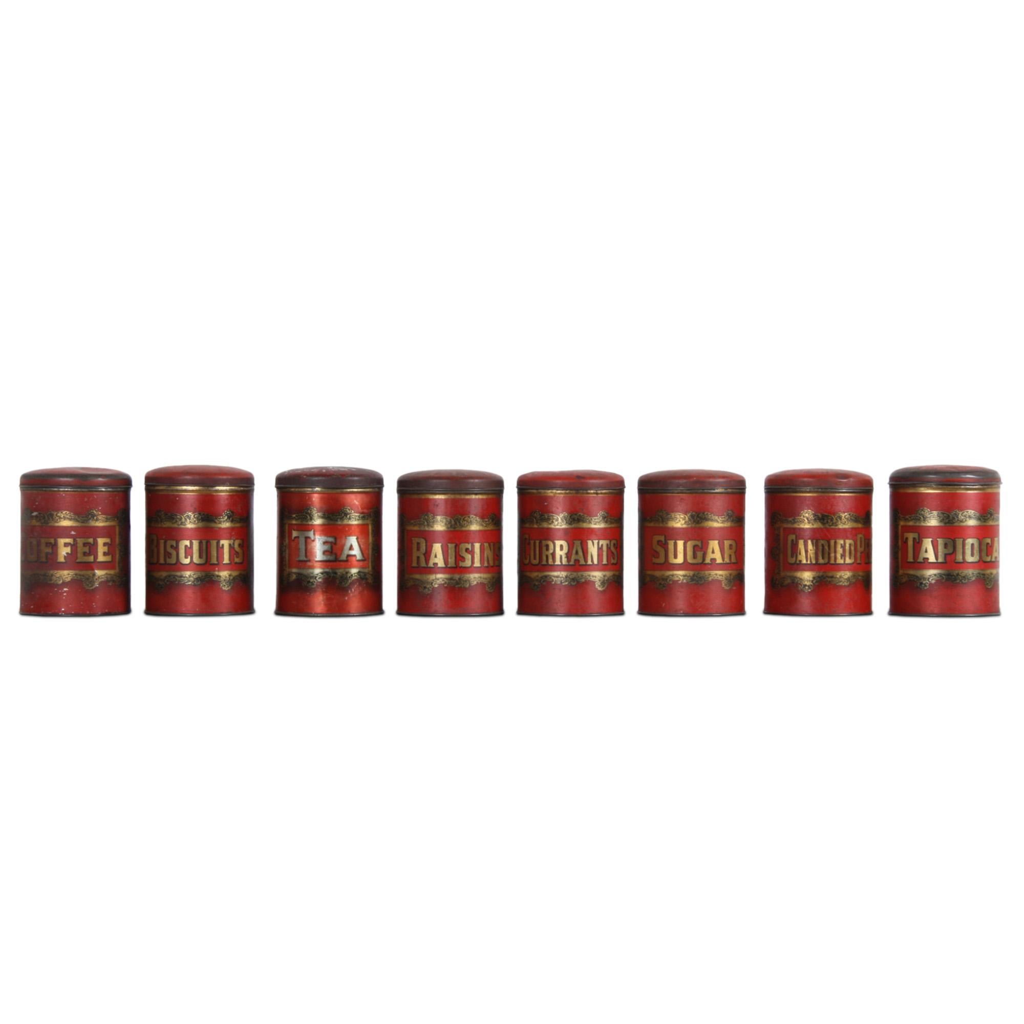 A set of 8 storage tins, these are made from polychrome and gilt metal with a bold gold label within a scrolling frame. A tin for tea, coffee, sugar, raisins, tapioca, biscuits, currants and candied peel. 

Decorative kitchenalia. 

Made in