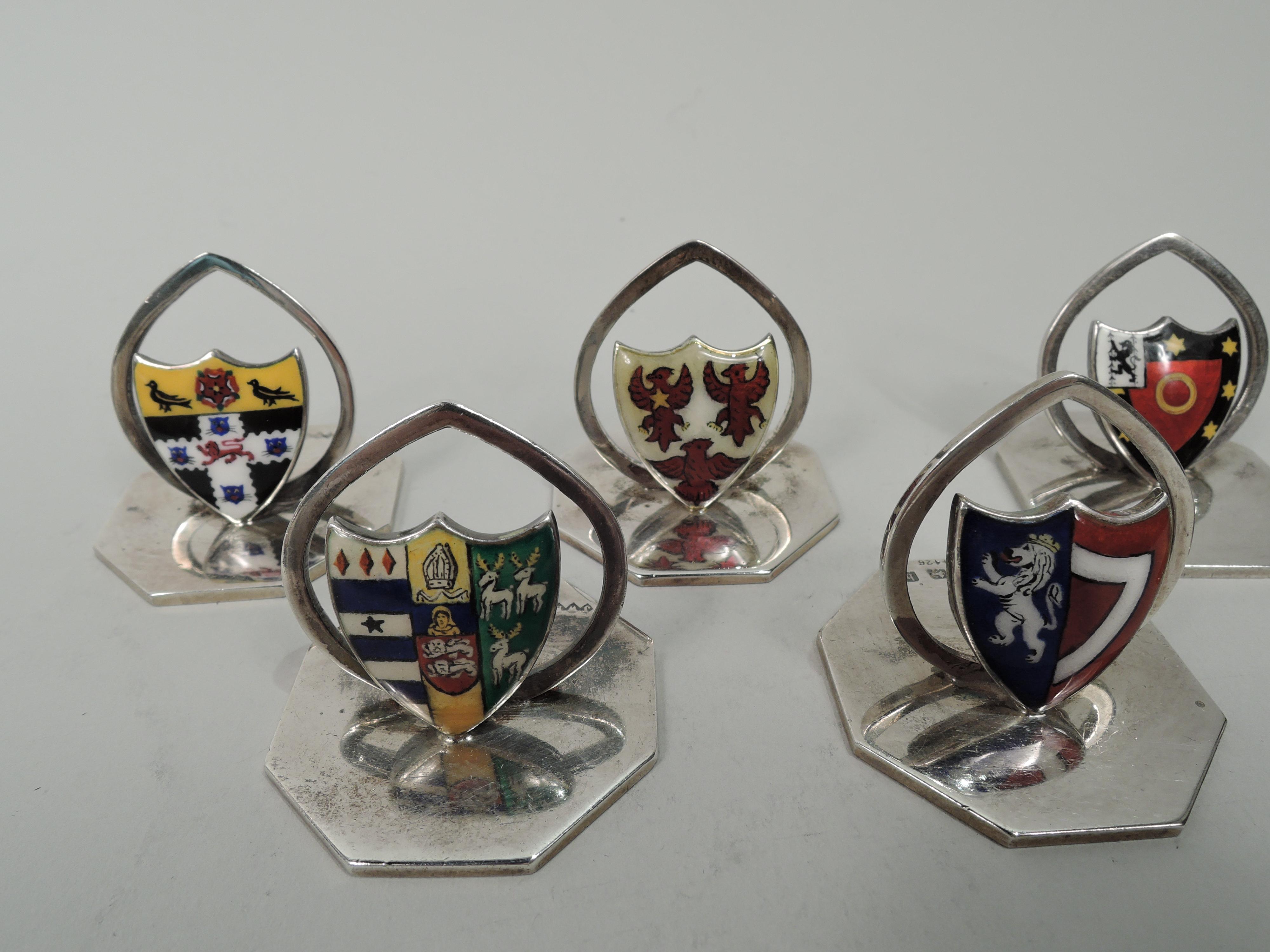 Set of 8 Edwardian sterling silver and enamel place card holders. Made by James William Benson in Birmingham, 1902 to 1909. Each: Enameled coat of arms and open oval clip mounted to flat octagonal base. Each coat of arms different. Symbols include