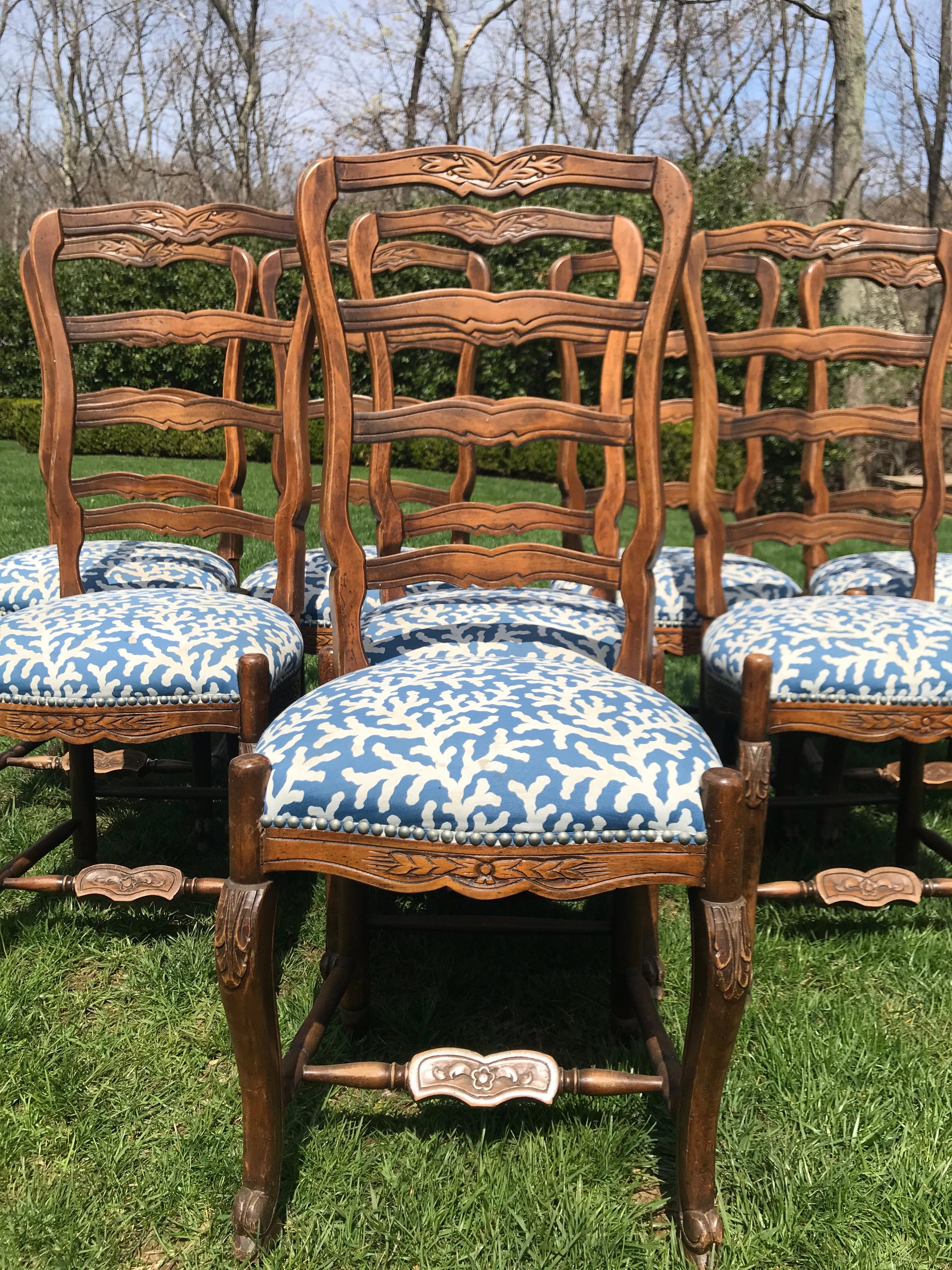 These French ladder back dining chairs have carved flowers on the top of the chair, sides, front. They have
cross-stretchers for added solidity which is adorned with a carved flower as well. Upholstered in
a blue and white coral pattern with