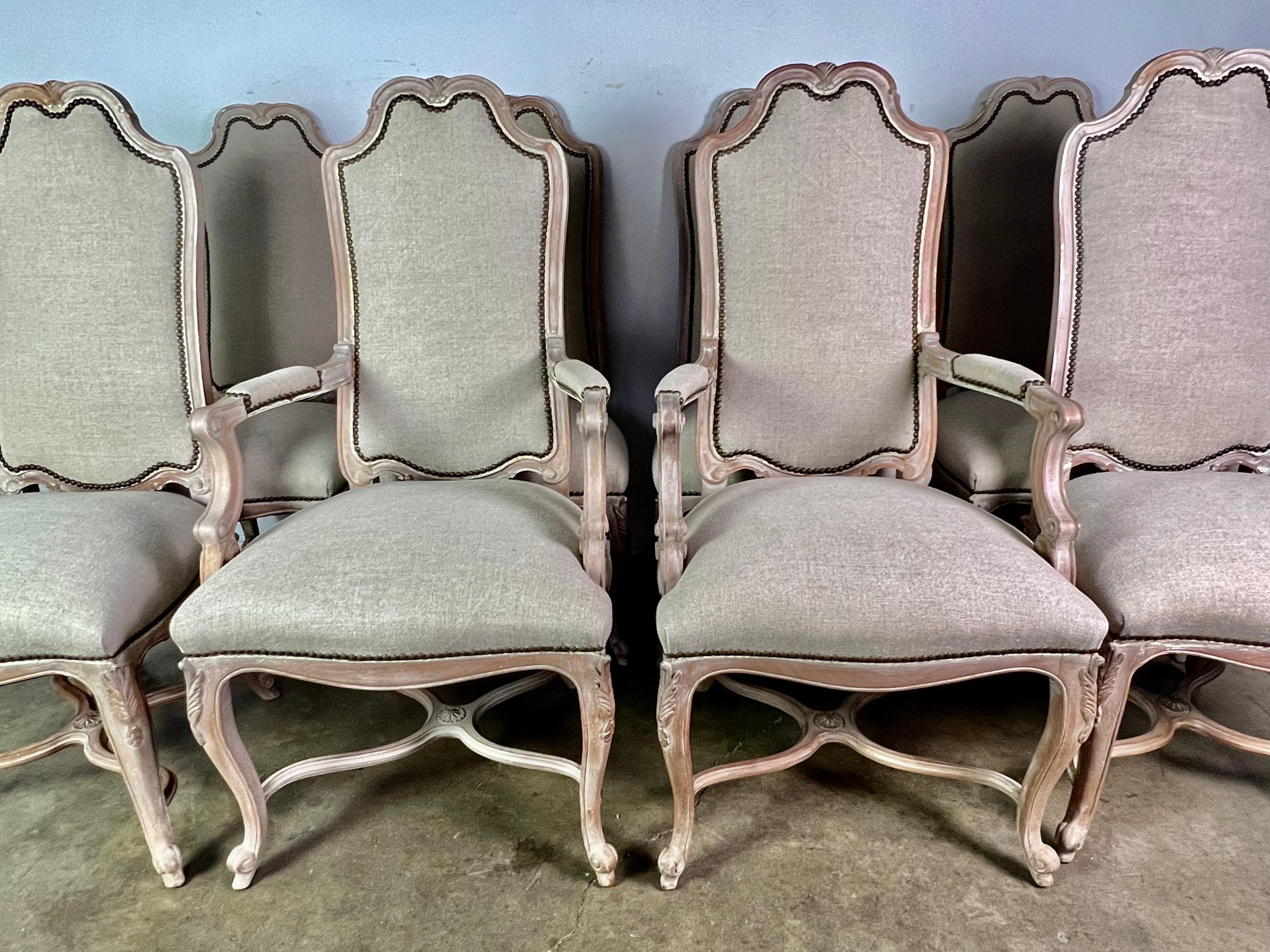 Set of (8) French Louis XV style dining chairs in a bleached walnut wood. The chairs are newly upholstered in a washed Belgium linen with nailhead trim detail. The chairs stand on four cabriole legs with rams head feet. The legs are all connected by