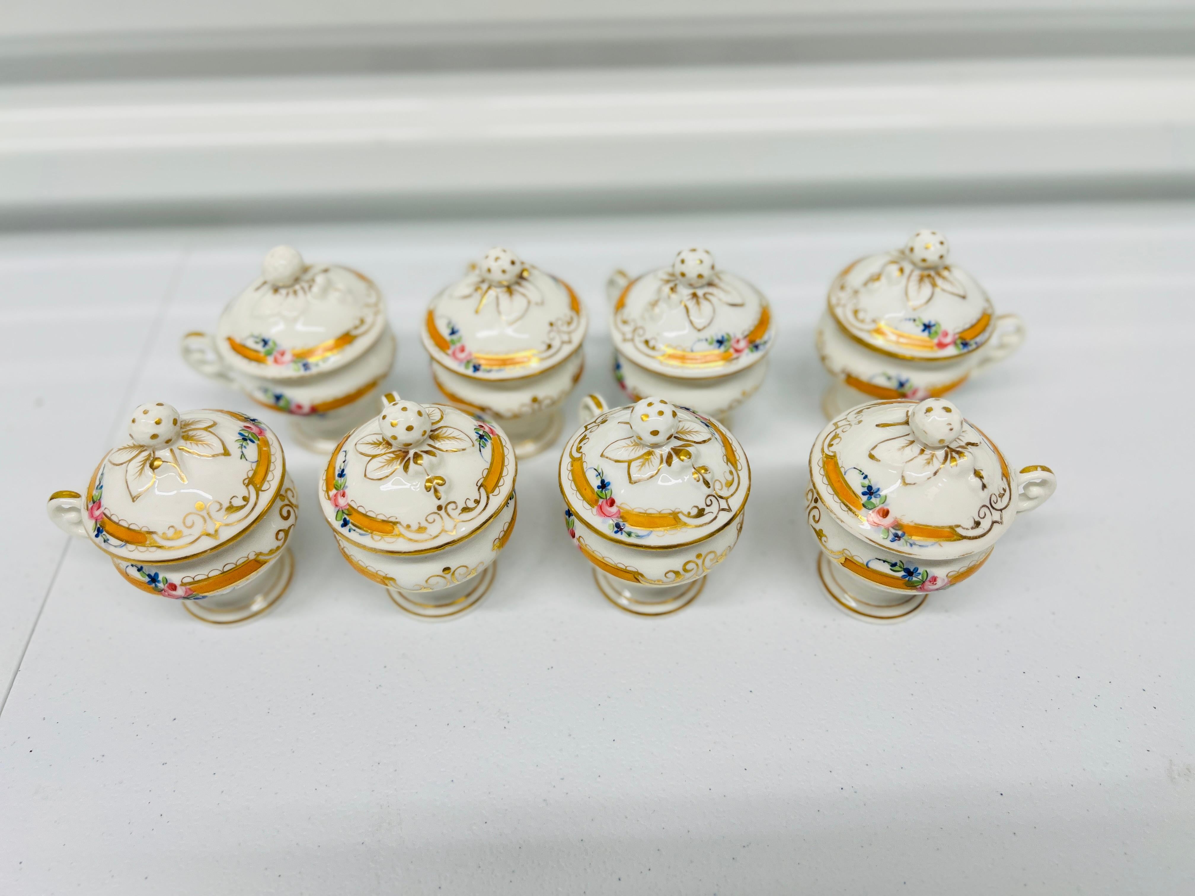 French Old Paris Porcelain, 19th century.

A set of 8 porcelain chocolate cups or pot de creme jars. Each features a white porcelain body accented by orange bands with gold accents, floral detailing, petite handles and a strawberry finial. Unmarked.