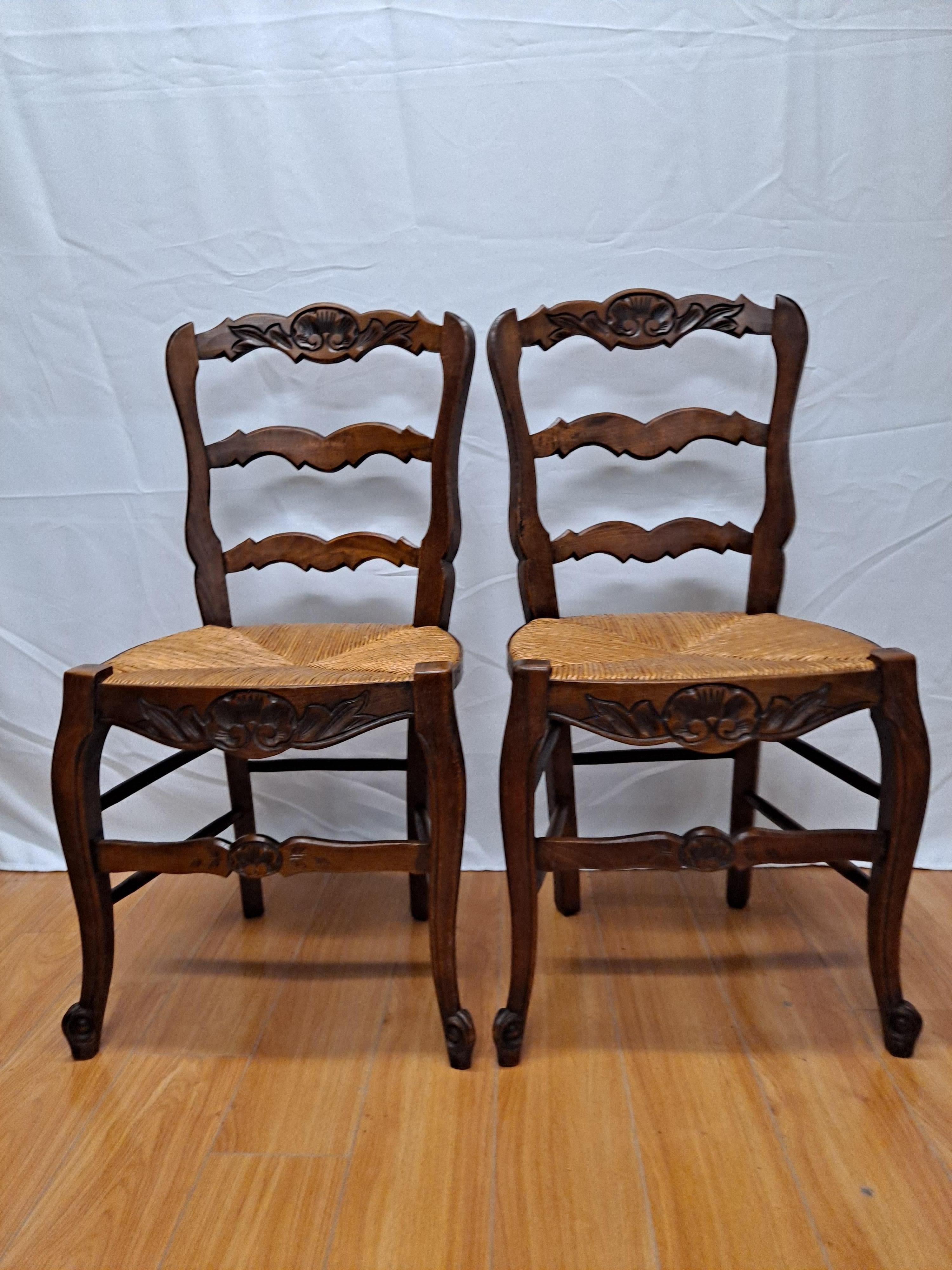Set of 8 French Provincial dining side chairs with rush seats, ladder backs, and beautifully hand carved traditional floral motifs. Wood is most likely walnut, but possibly oak.