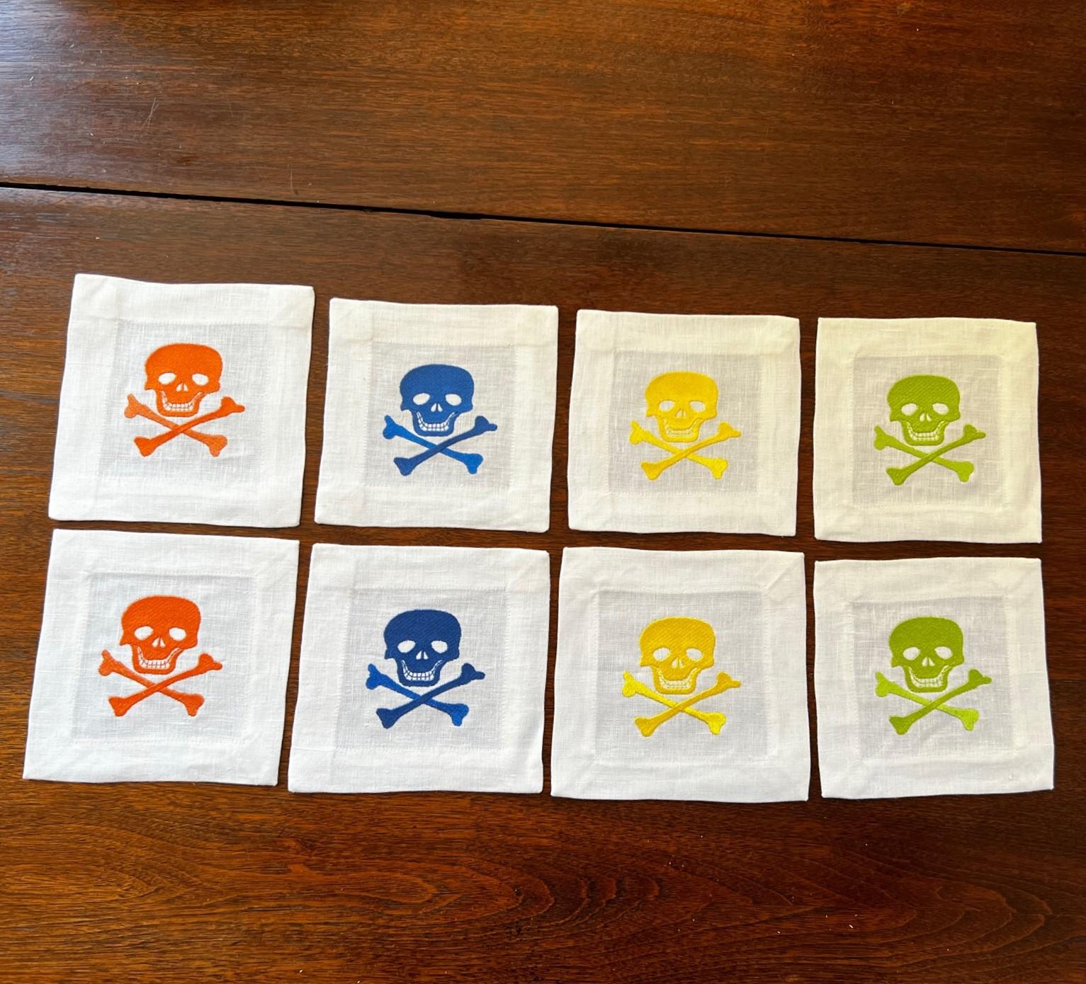 Late 20th C, American, a set of 8 white linen cocktail napkins embroidered with skull and crossbones; 2 each of orange, blue, green and gold.

Dimensions:
6