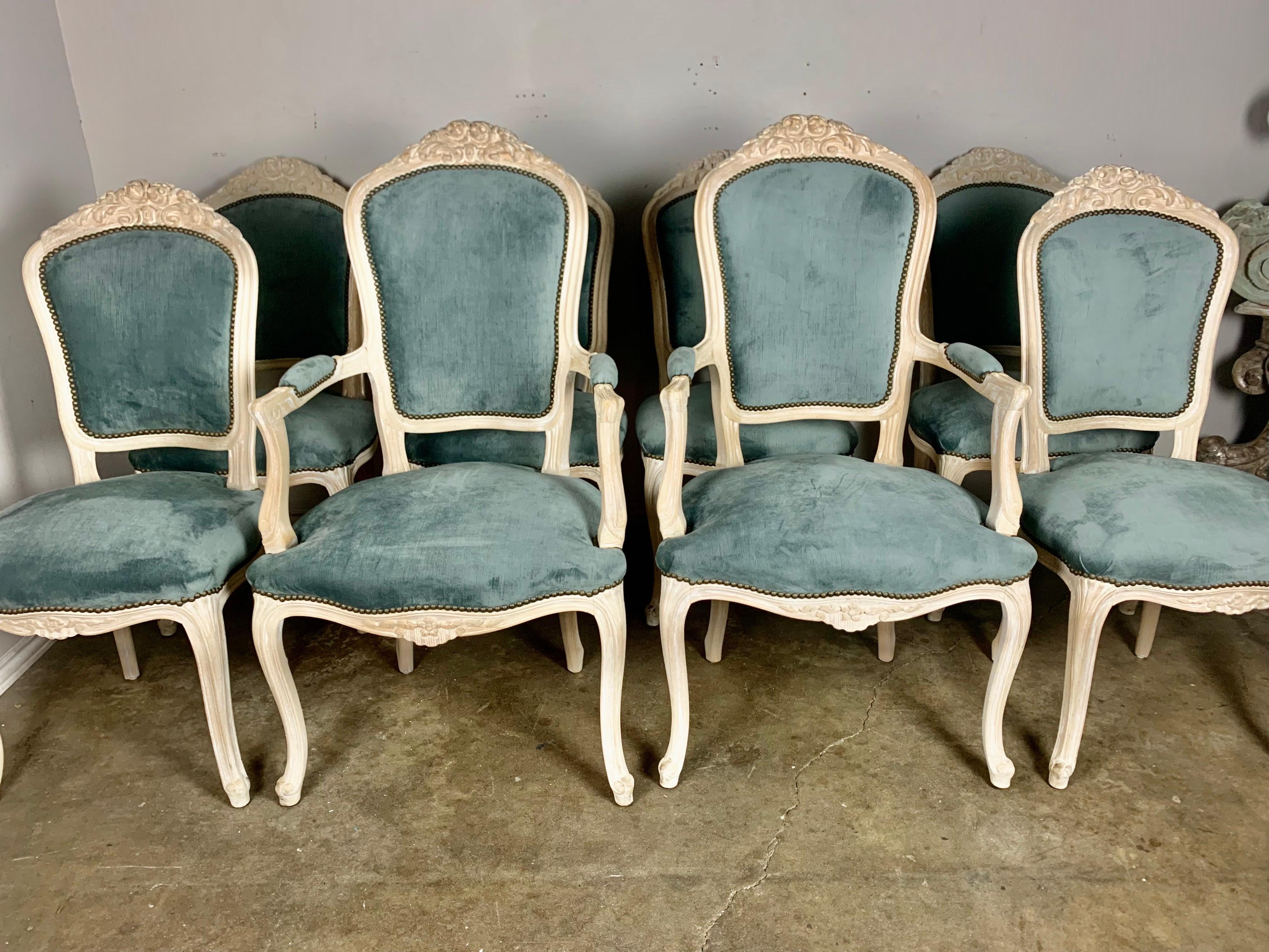 Set of eight bleached walnut Louis XV style dining chairs with carved roses and flowers throughout. The chairs have beautiful oval shaped backs and stand on four cabriole legs with rams head feet. They are newly upholstered in a steel blue colored
