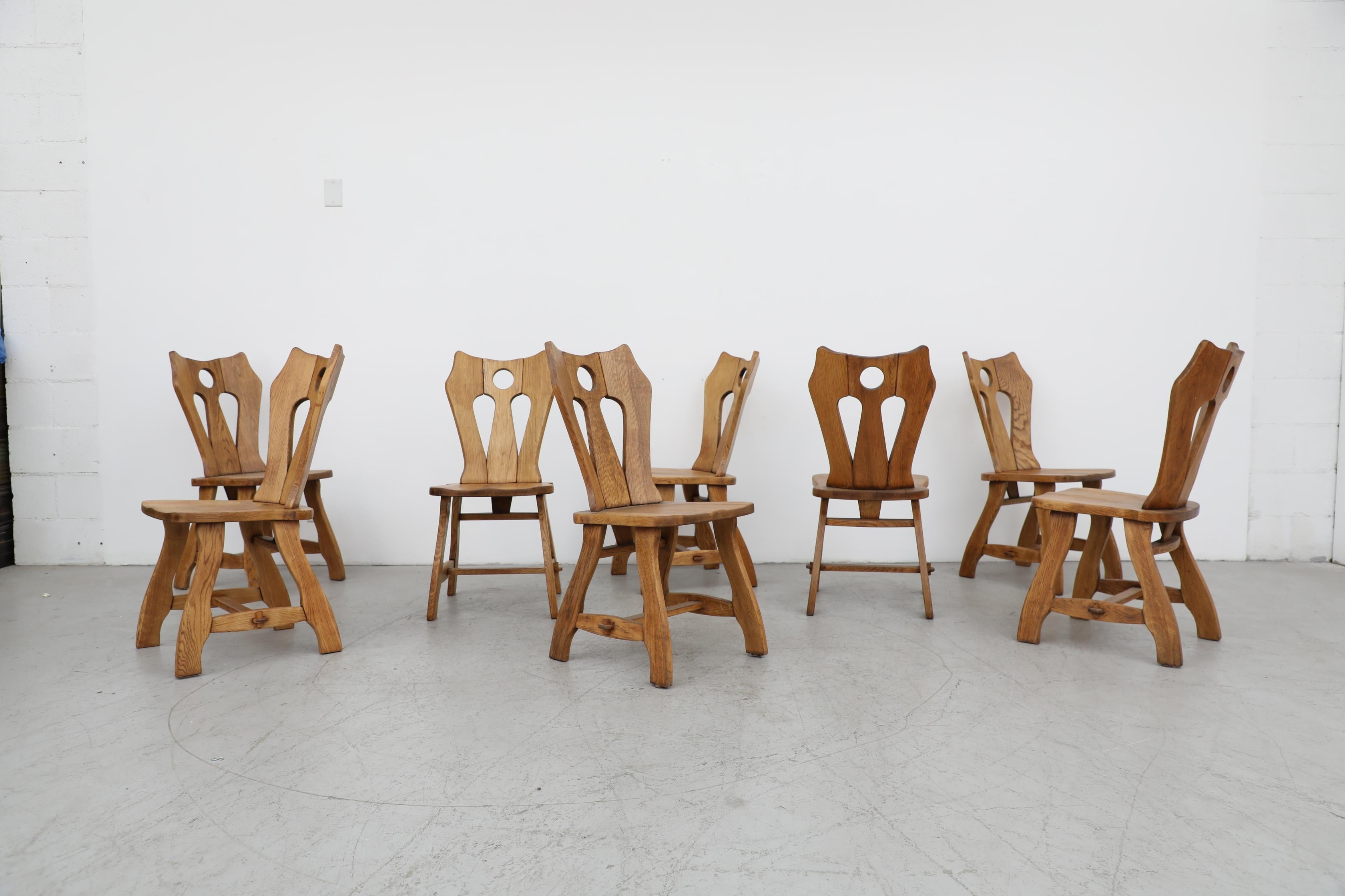 Beautiful Brutalist set of 8 De Puydt solid oak dining chairs with ornately carved backrests. Lightly refinished in otherwise original condition with visible wear, including some missing pegs. Wear is consistent with their age and use.