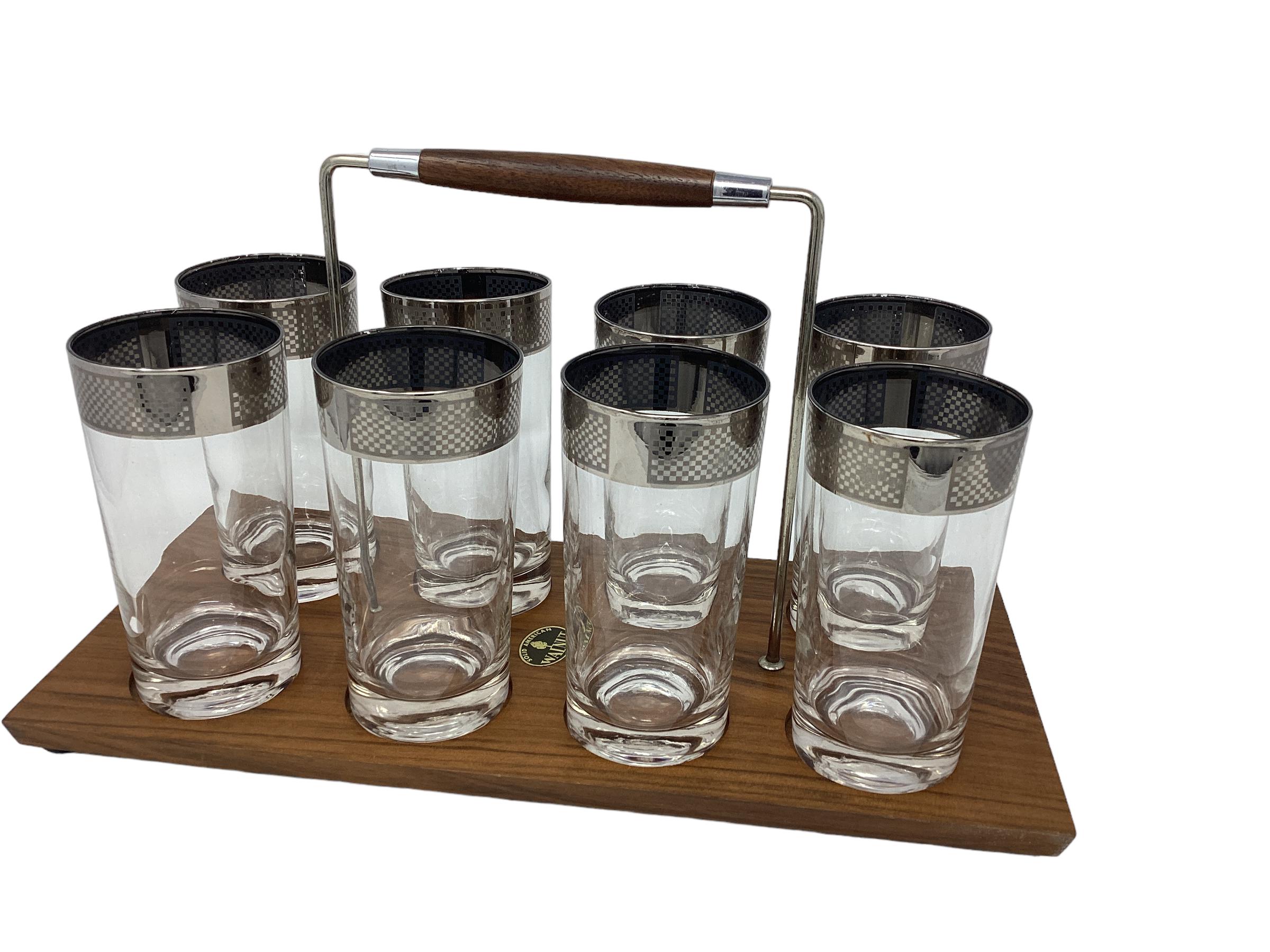 Set of 8 highball glasses. Each with a wide silver band in a checker board design. Comes with original walnut and chrome carrier.